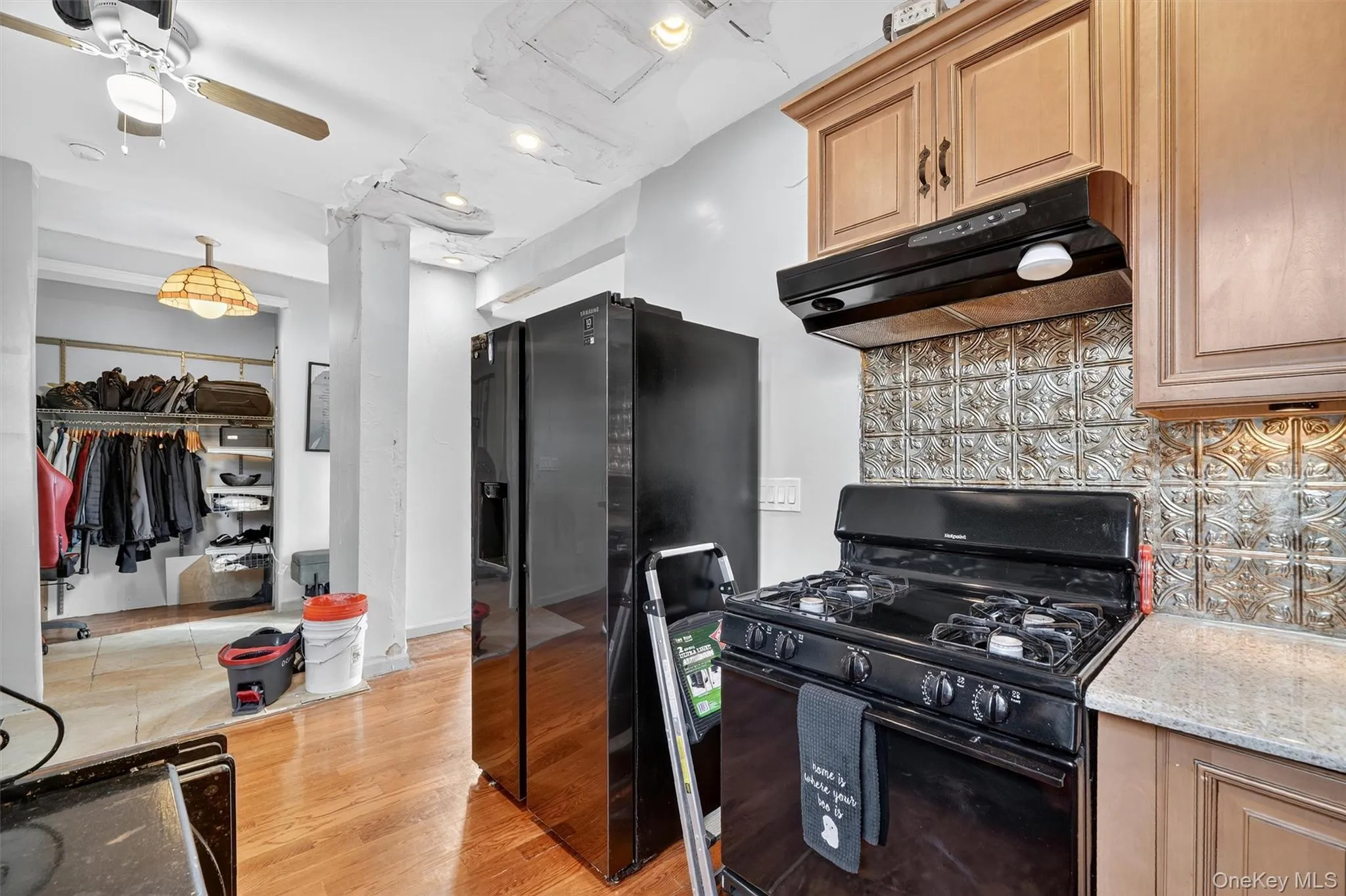 Kitchen featuring black appliances, tasteful backsplash, under cabinet range hood, light wood-style flooring, and light stone countertops Kitchen featuring black appliances, tasteful backsplash, under cabinet range hood, light wood-style flooring, and light stone countertops