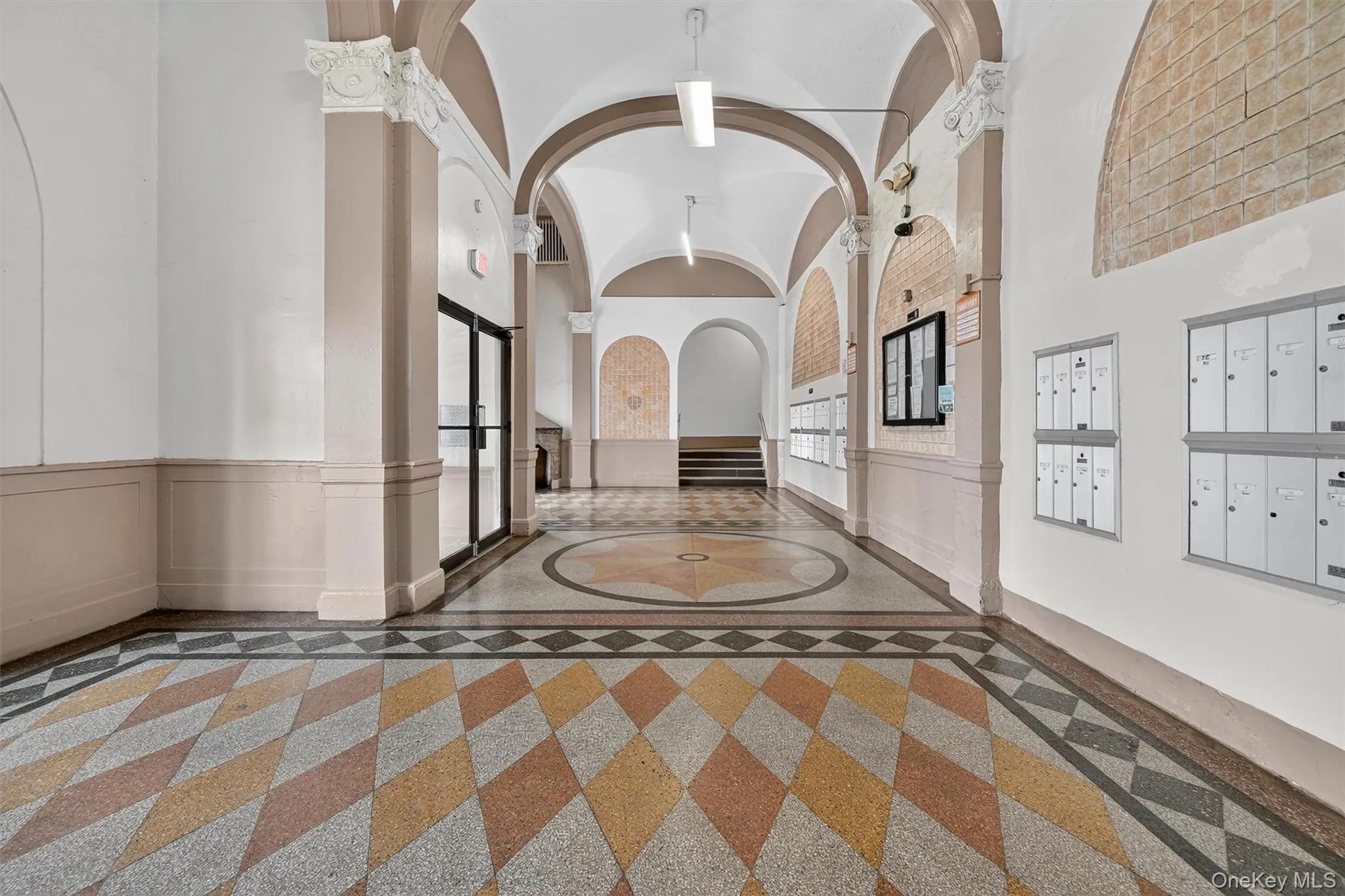 Hallway featuring inlaid floor details, a wainscoted wall, a high ceiling, and mail area Hallway featuring inlaid floor details, a wainscoted wall, a high ceiling, and mail area