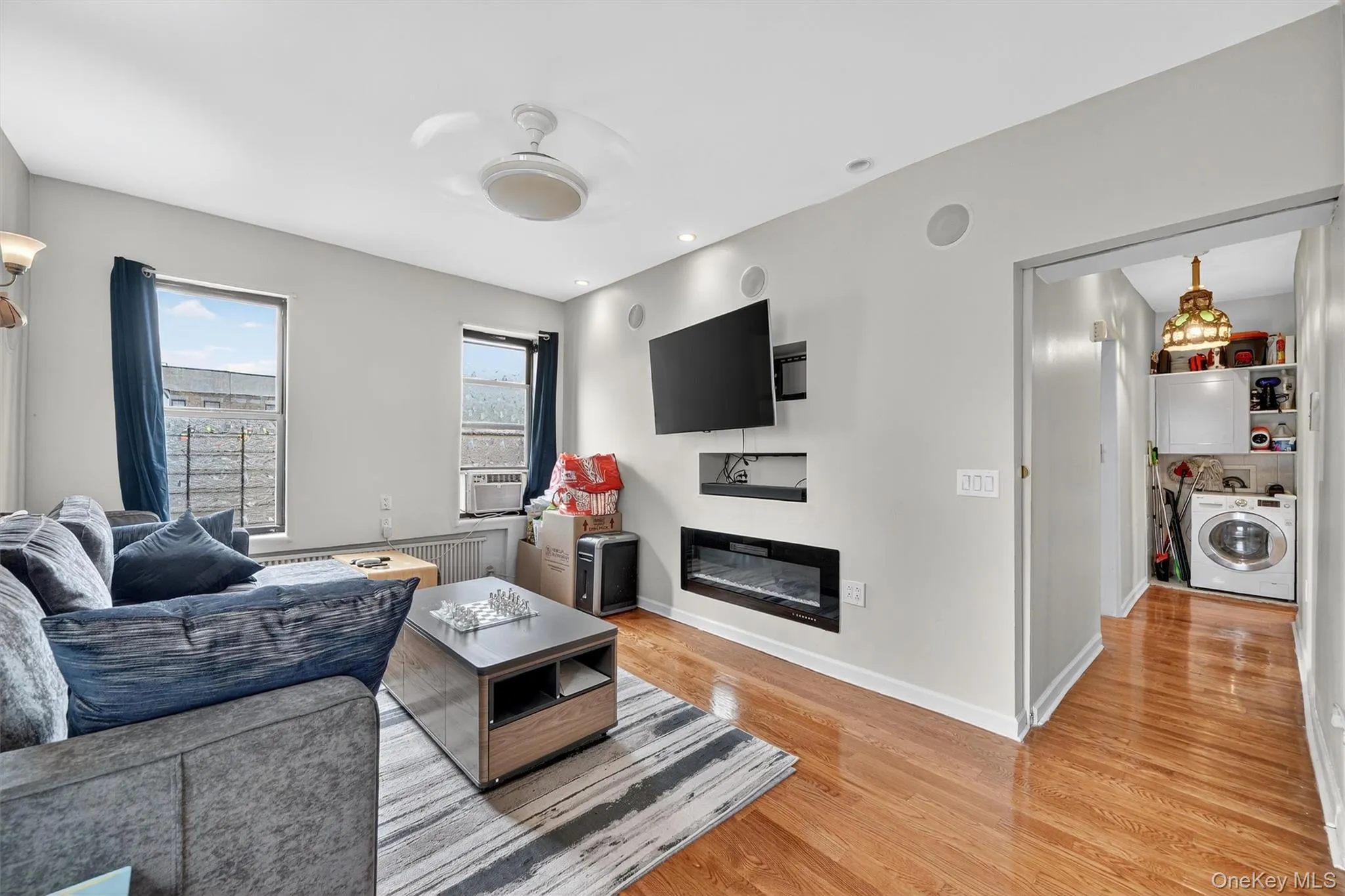 Living room with washer / dryer, a glass covered fireplace, light wood-type flooring, radiator, and a ceiling fan Living room with washer / dryer, a glass covered fireplace, light wood-type flooring, radiator, and a ceiling fan