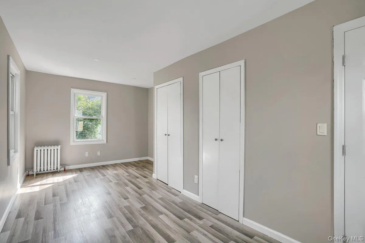 Unfurnished bedroom with two closets, radiator heating unit, and light wood-type flooring Unfurnished bedroom with two closets, radiator heating unit, and light wood-type flooring