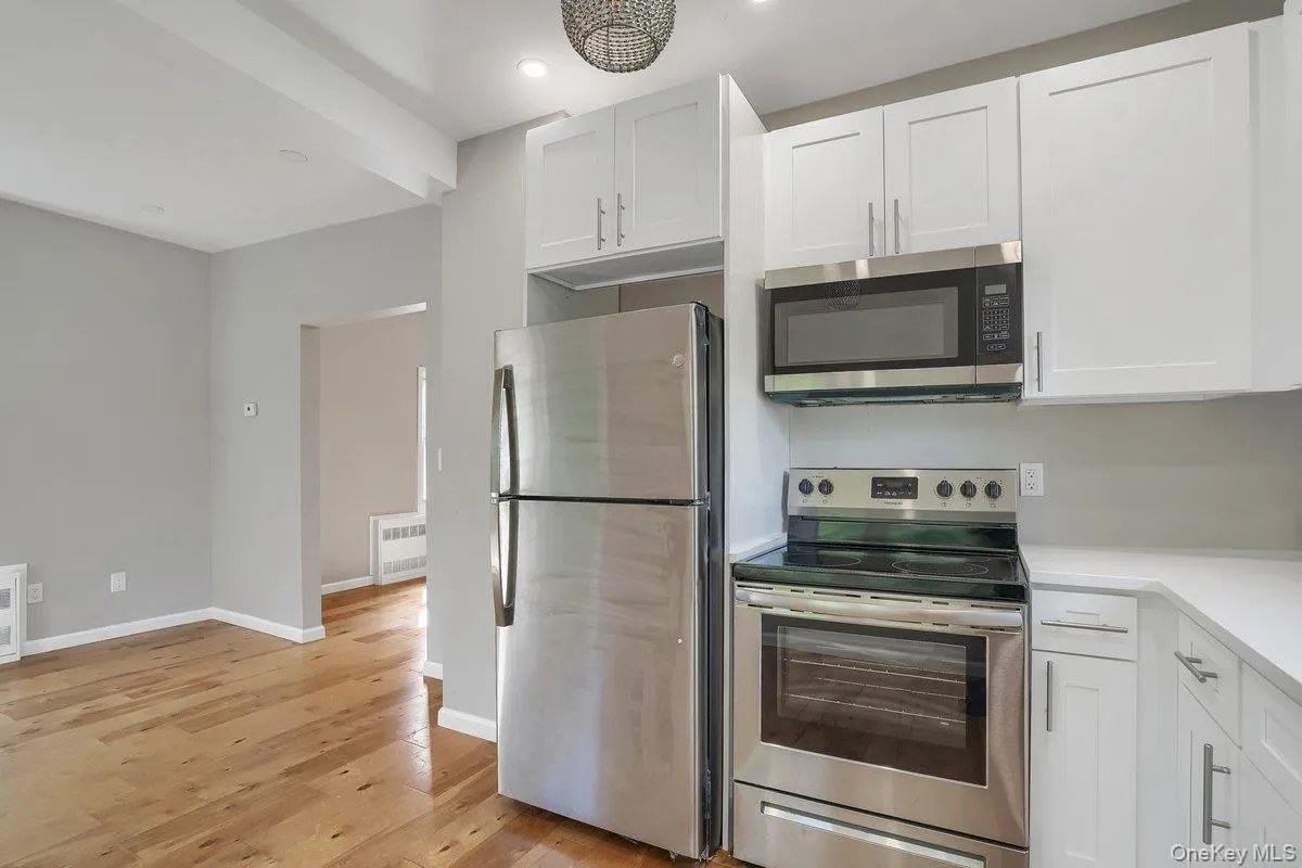 Kitchen featuring appliances with stainless steel finishes, white cabinetry, light wood-style flooring, beam ceiling, and radiator Kitchen featuring appliances with stainless steel finishes, white cabinetry, light wood-style flooring, beam ceiling, and radiator