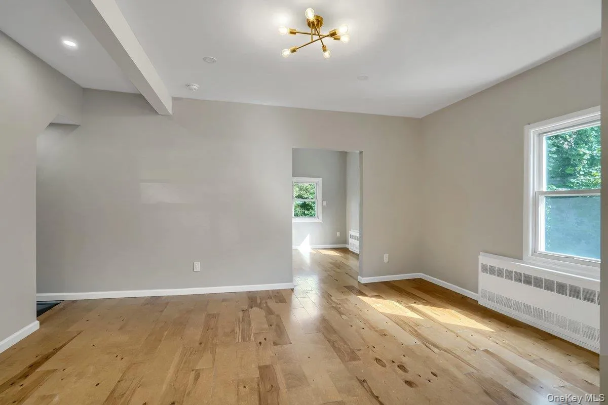 Spare room with radiator, light wood finished floors, a chandelier, and beam ceiling Spare room with radiator, light wood finished floors, a chandelier, and beam ceiling