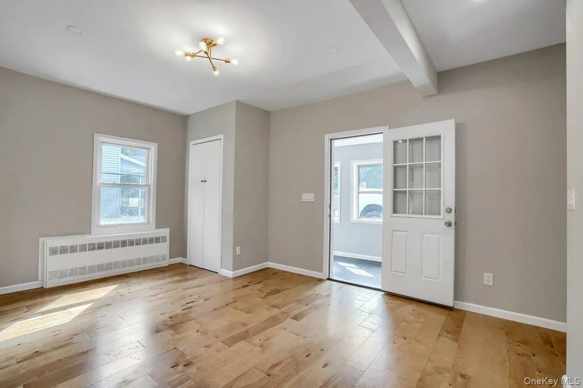 Unfurnished room featuring light wood-style floors, radiator, beam ceiling, and a chandelier Unfurnished room featuring light wood-style floors, radiator, beam ceiling, and a chandelier