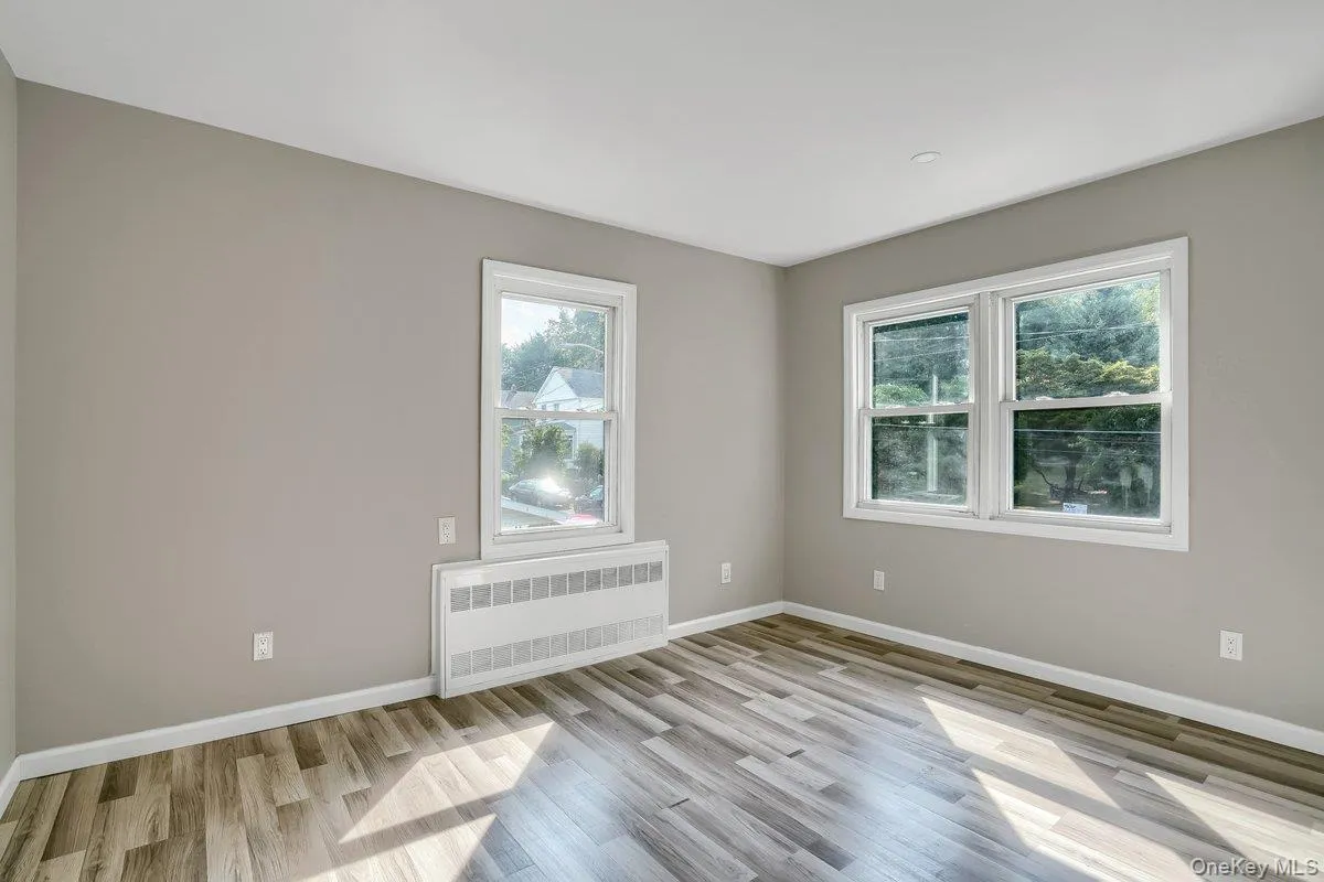 Unfurnished room featuring radiator, plenty of natural light, and light wood-style floors Unfurnished room featuring radiator, plenty of natural light, and light wood-style floors