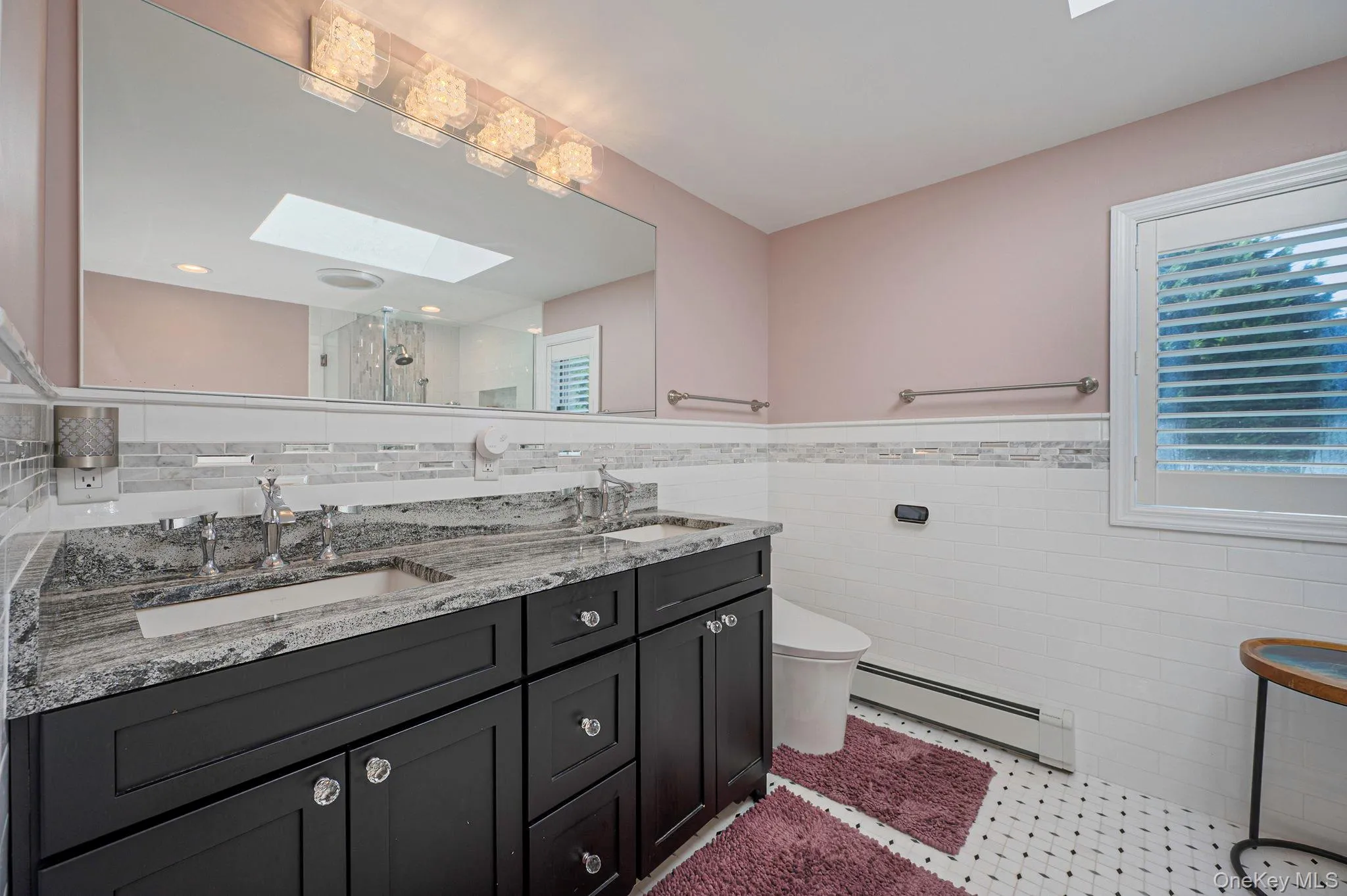 Bathroom with a skylight, baseboard heating, double vanity, a stall shower, and tile walls Bathroom with a skylight, baseboard heating, double vanity, a stall shower, and tile walls