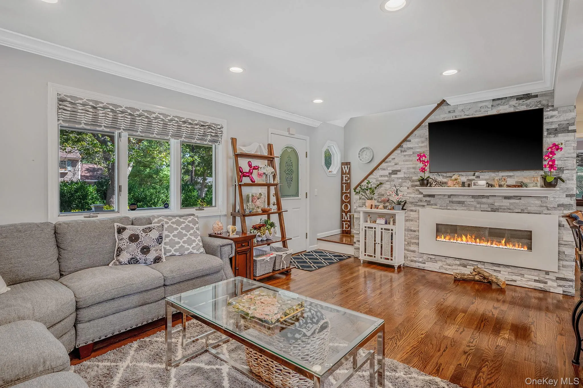 Living room with crown molding, wood finished floors, recessed lighting, and a stone fireplace Living room with crown molding, wood finished floors, recessed lighting, and a stone fireplace