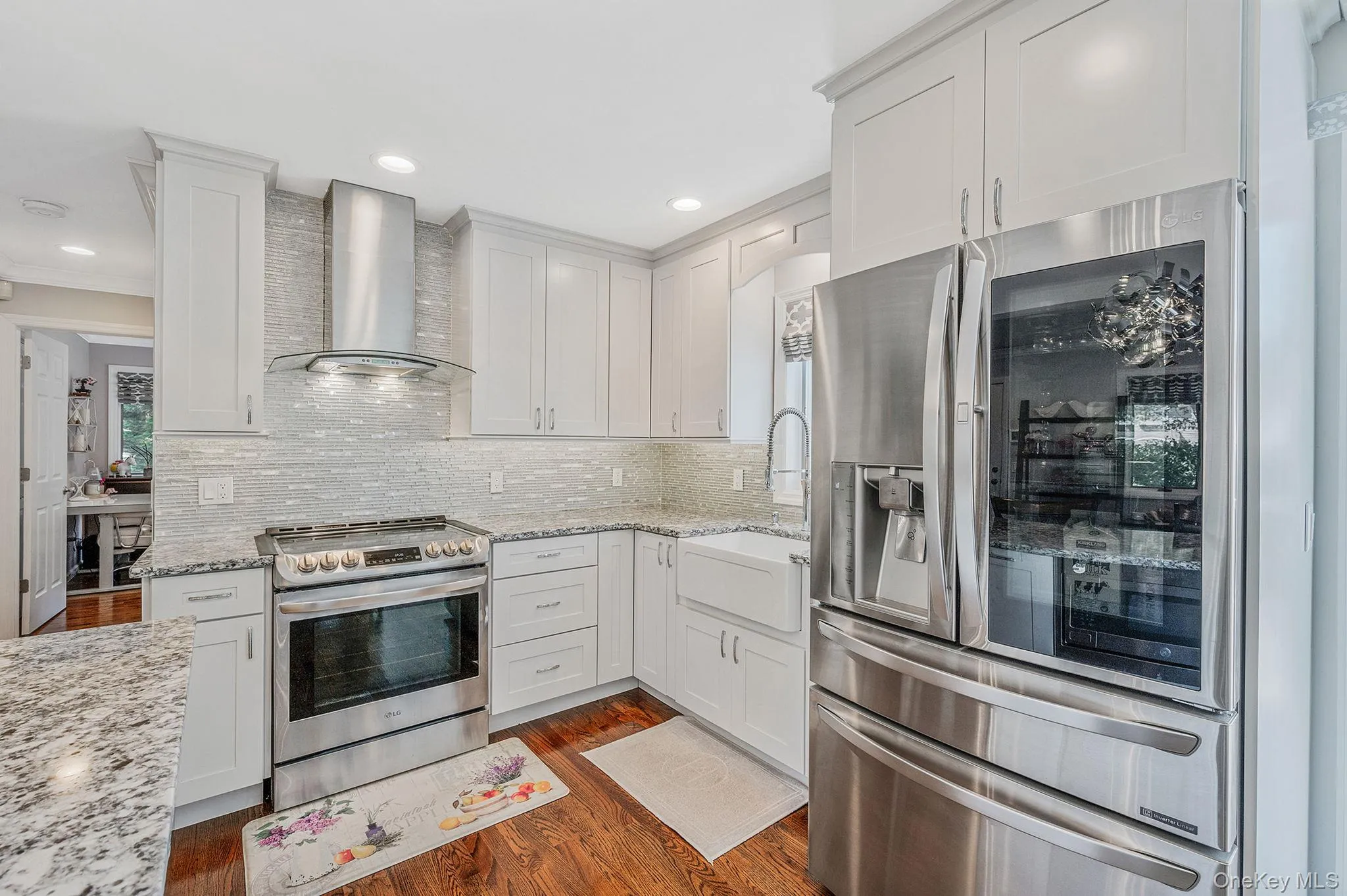 Kitchen with stainless steel appliances, wall chimney range hood, white cabinetry, dark wood-style floors, and light stone counters Kitchen with stainless steel appliances, wall chimney range hood, white cabinetry, dark wood-style floors, and light stone counters
