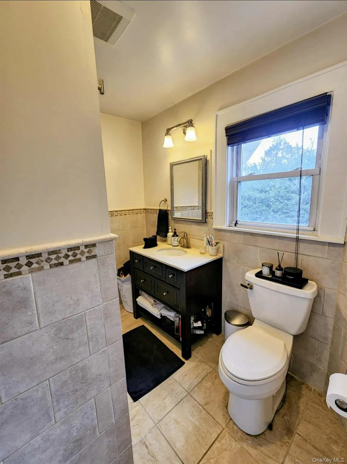 Bathroom featuring tile walls, vanity, a wainscoted wall, and light tile patterned floors Bathroom featuring tile walls, vanity, a wainscoted wall, and light tile patterned floors