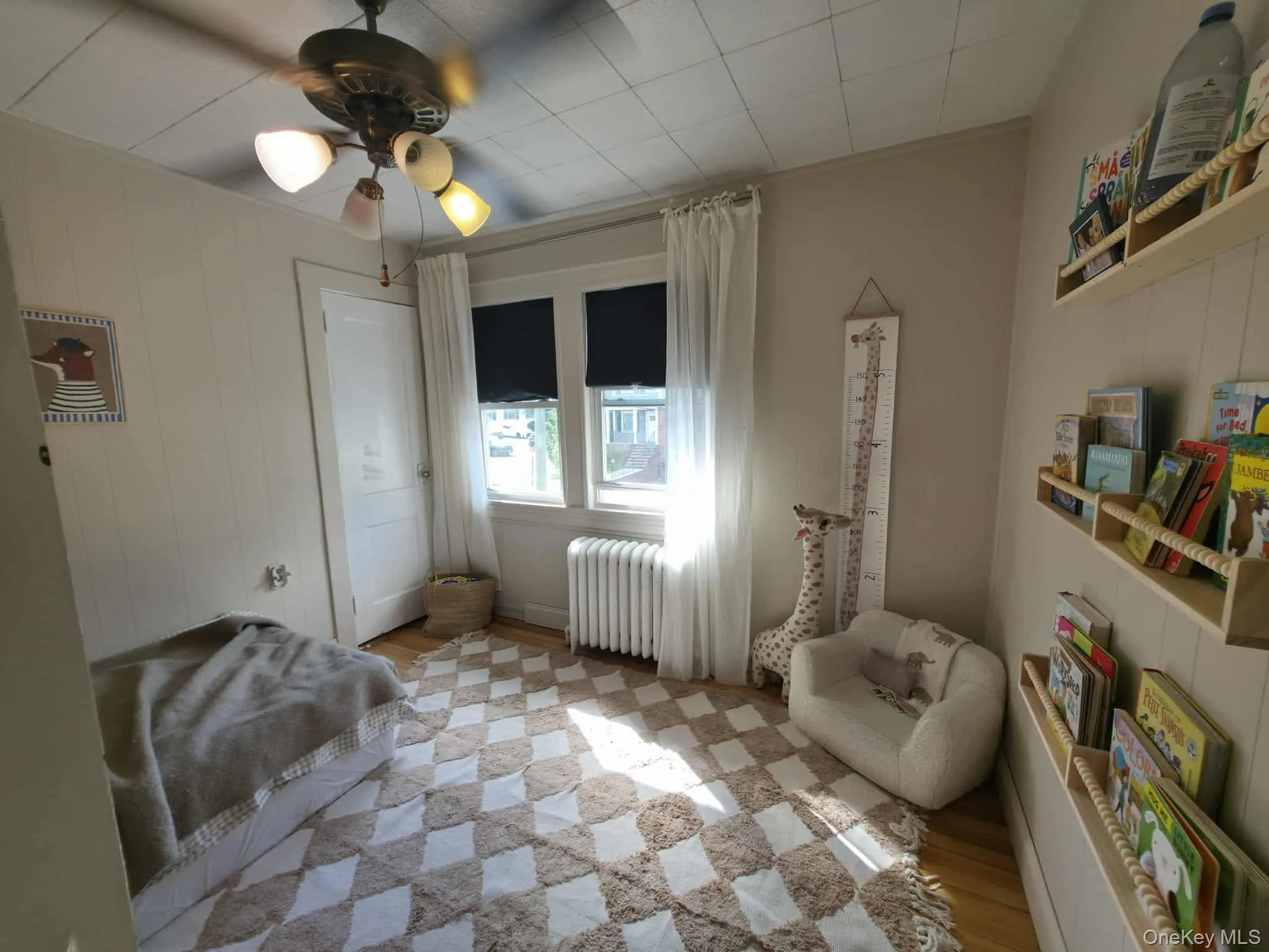 Bedroom featuring wood finished floors, radiator heating unit, ceiling fan, and wooden walls Bedroom featuring wood finished floors, radiator heating unit, ceiling fan, and wooden walls