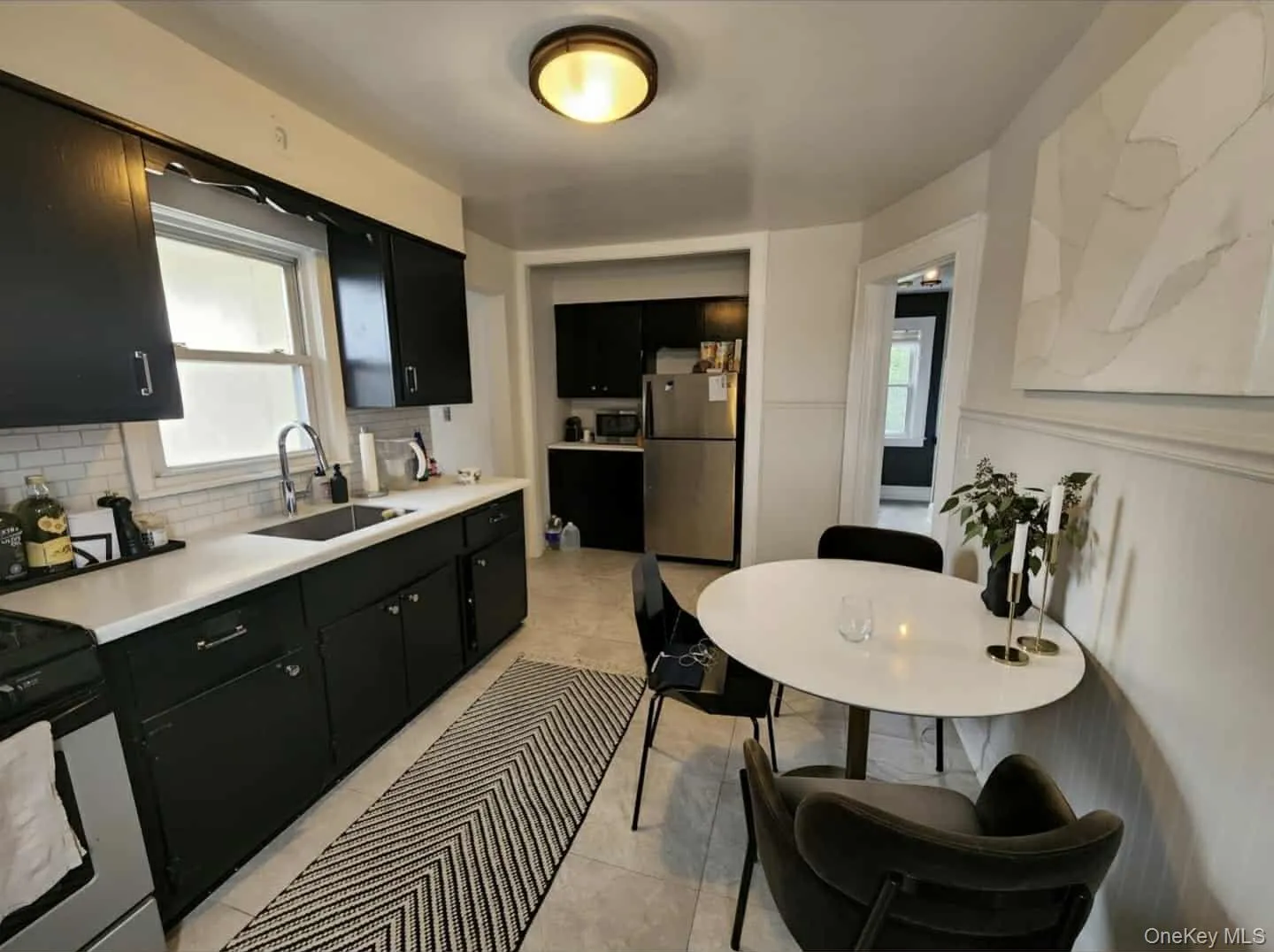 Kitchen featuring dark cabinets, light countertops, stainless steel appliances, decorative backsplash, and light tile patterned floors Kitchen featuring dark cabinets, light countertops, stainless steel appliances, decorative backsplash, and light tile patterned floors