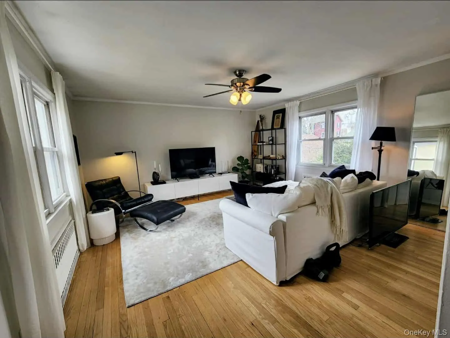 Living area with ornamental molding, light wood-type flooring, ceiling fan, a baseboard radiator, and radiator Living area with ornamental molding, light wood-type flooring, ceiling fan, a baseboard radiator, and radiator