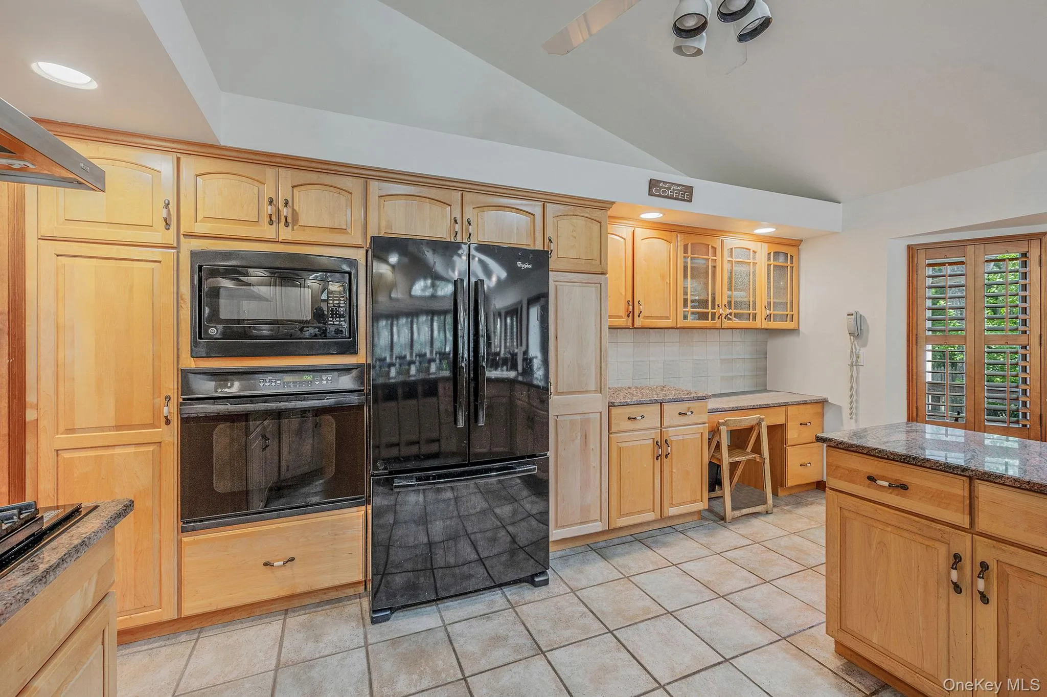 Kitchen with black appliances, dark stone counters, light tile patterned floors, decorative backsplash, and vaulted ceiling Kitchen with black appliances, dark stone counters, light tile patterned floors, decorative backsplash, and vaulted ceiling