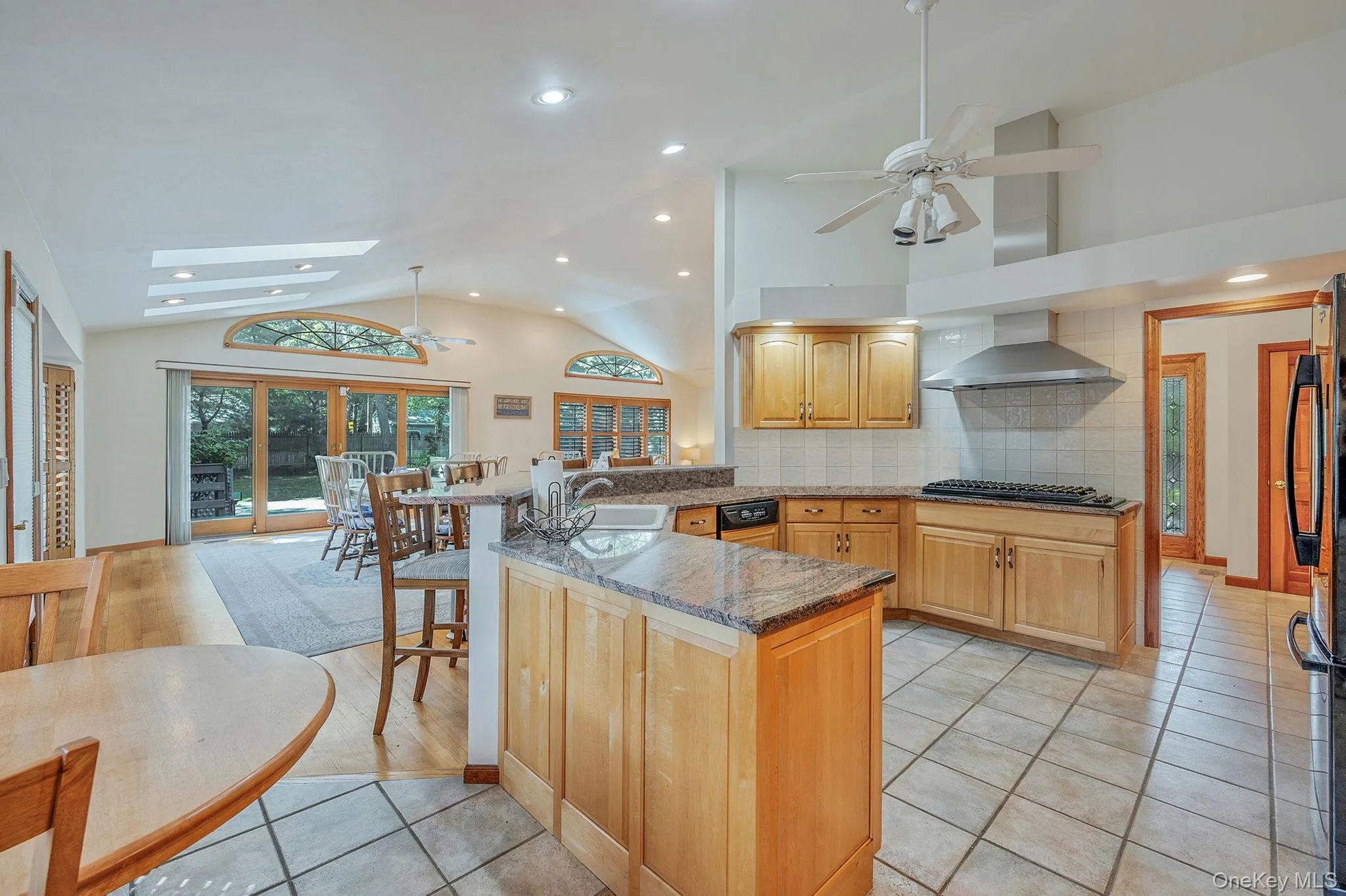 Kitchen with a ceiling fan, light tile patterned floors, a kitchen breakfast bar, a skylight, and backsplash Kitchen with a ceiling fan, light tile patterned floors, a kitchen breakfast bar, a skylight, and backsplash