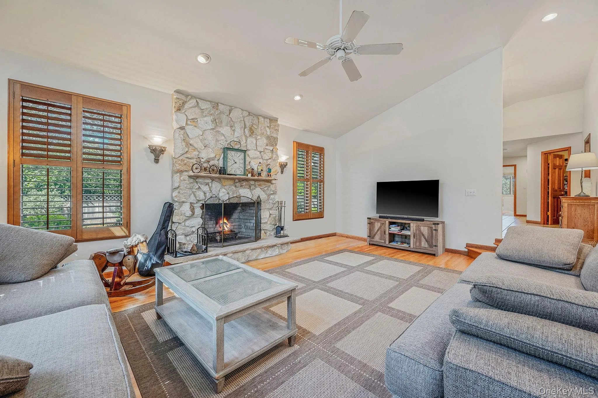 Living area featuring light wood-style floors, a stone fireplace, recessed lighting, a ceiling fan, and high vaulted ceiling Living area featuring light wood-style floors, a stone fireplace, recessed lighting, a ceiling fan, and high vaulted ceiling