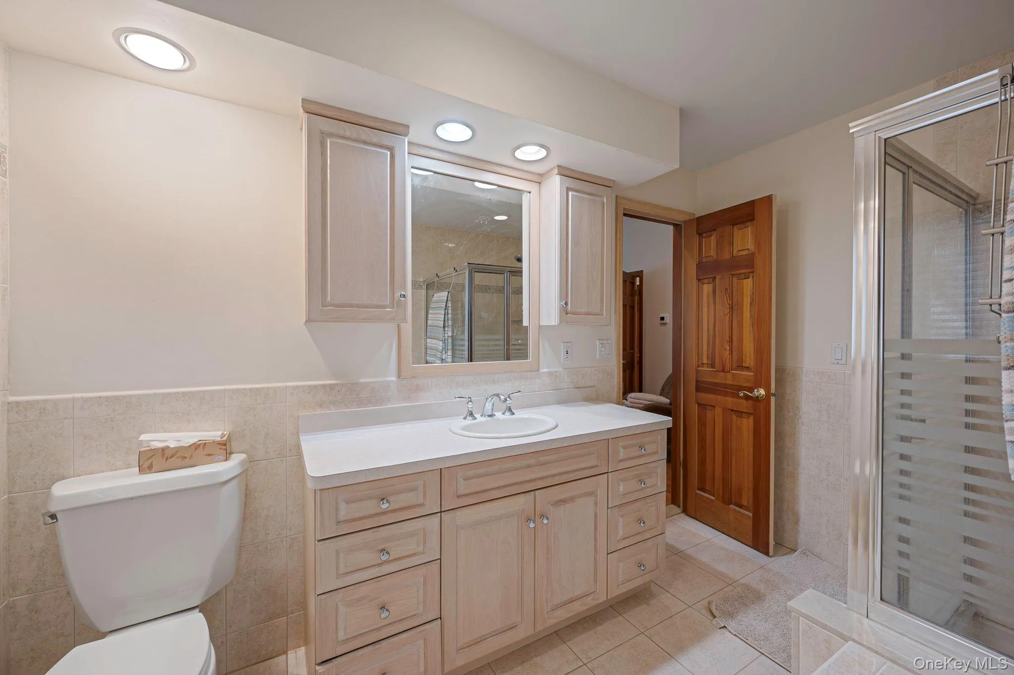 Bathroom with tile walls, a wainscoted wall, light tile patterned floors, a stall shower, and vanity Bathroom with tile walls, a wainscoted wall, light tile patterned floors, a stall shower, and vanity