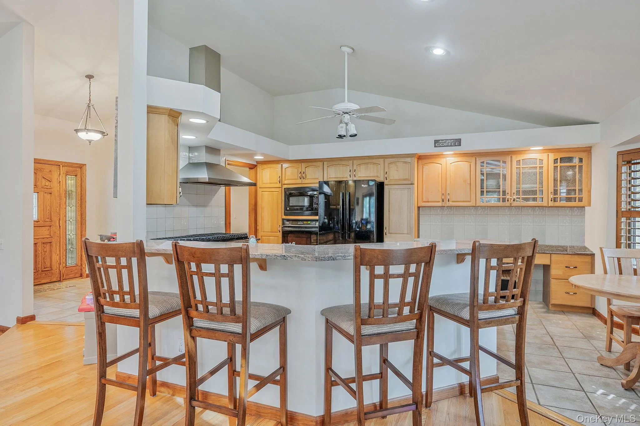 Kitchen featuring backsplash, black appliances, glass insert cabinets, recessed lighting, and wall chimney exhaust hood Kitchen featuring backsplash, black appliances, glass insert cabinets, recessed lighting, and wall chimney exhaust hood