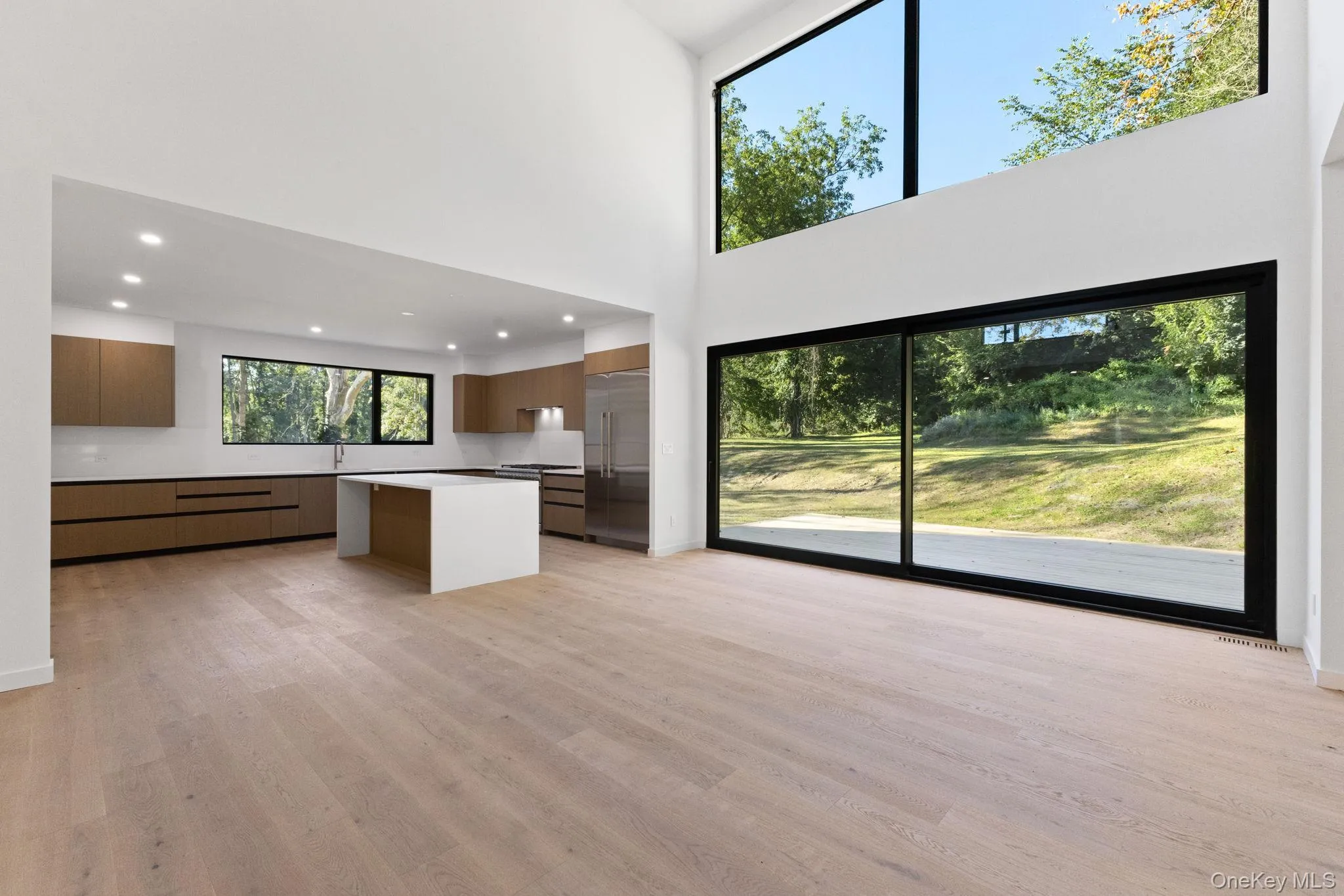 Kitchen featuring modern cabinets, brown cabinetry, light wood-style flooring, a high ceiling, and built in fridge Kitchen featuring modern cabinets, brown cabinetry, light wood-style flooring, a high ceiling, and built in fridge