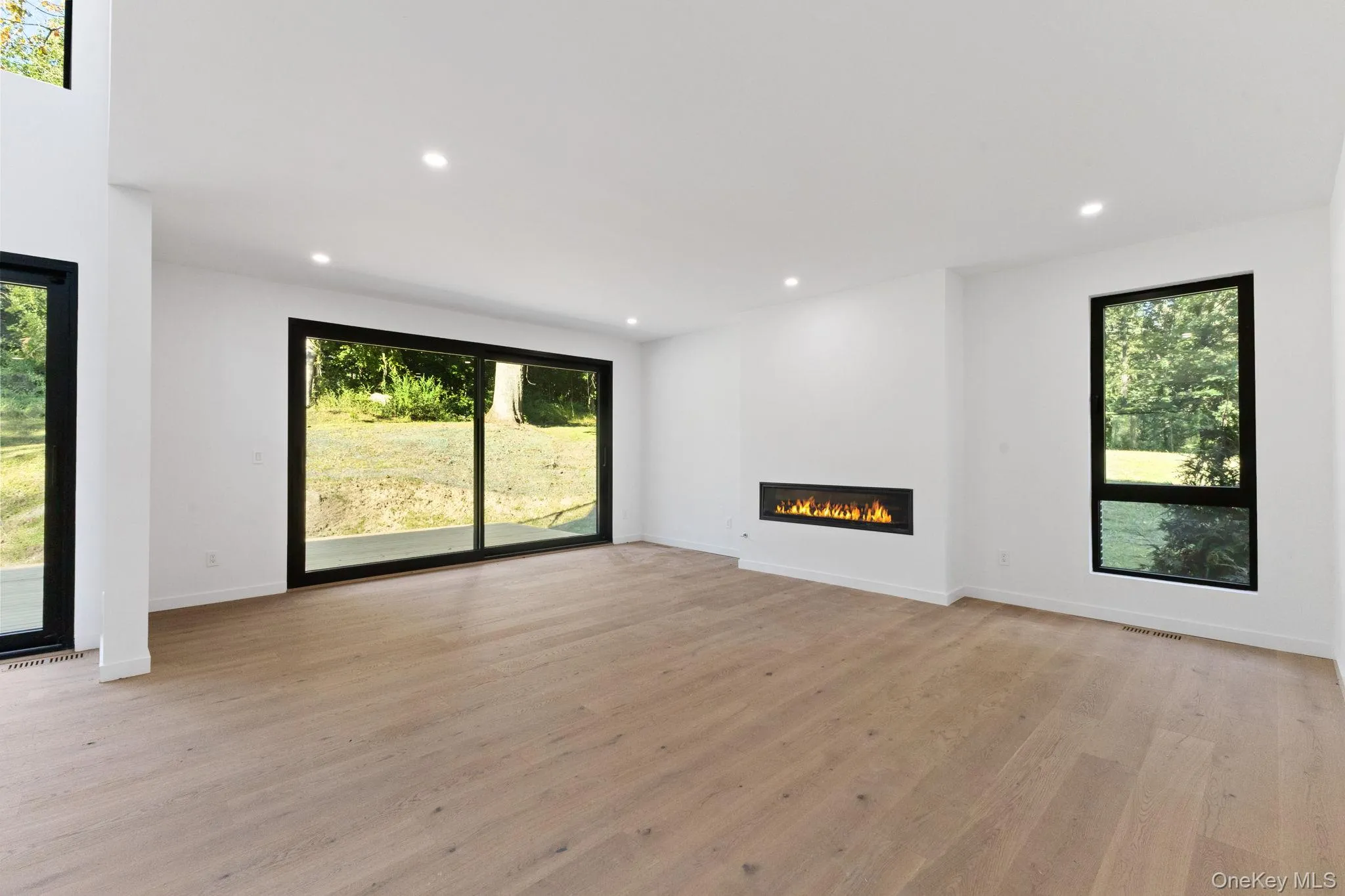 Unfurnished living room featuring a glass covered fireplace, light wood-type flooring, and recessed lighting Unfurnished living room featuring a glass covered fireplace, light wood-type flooring, and recessed lighting