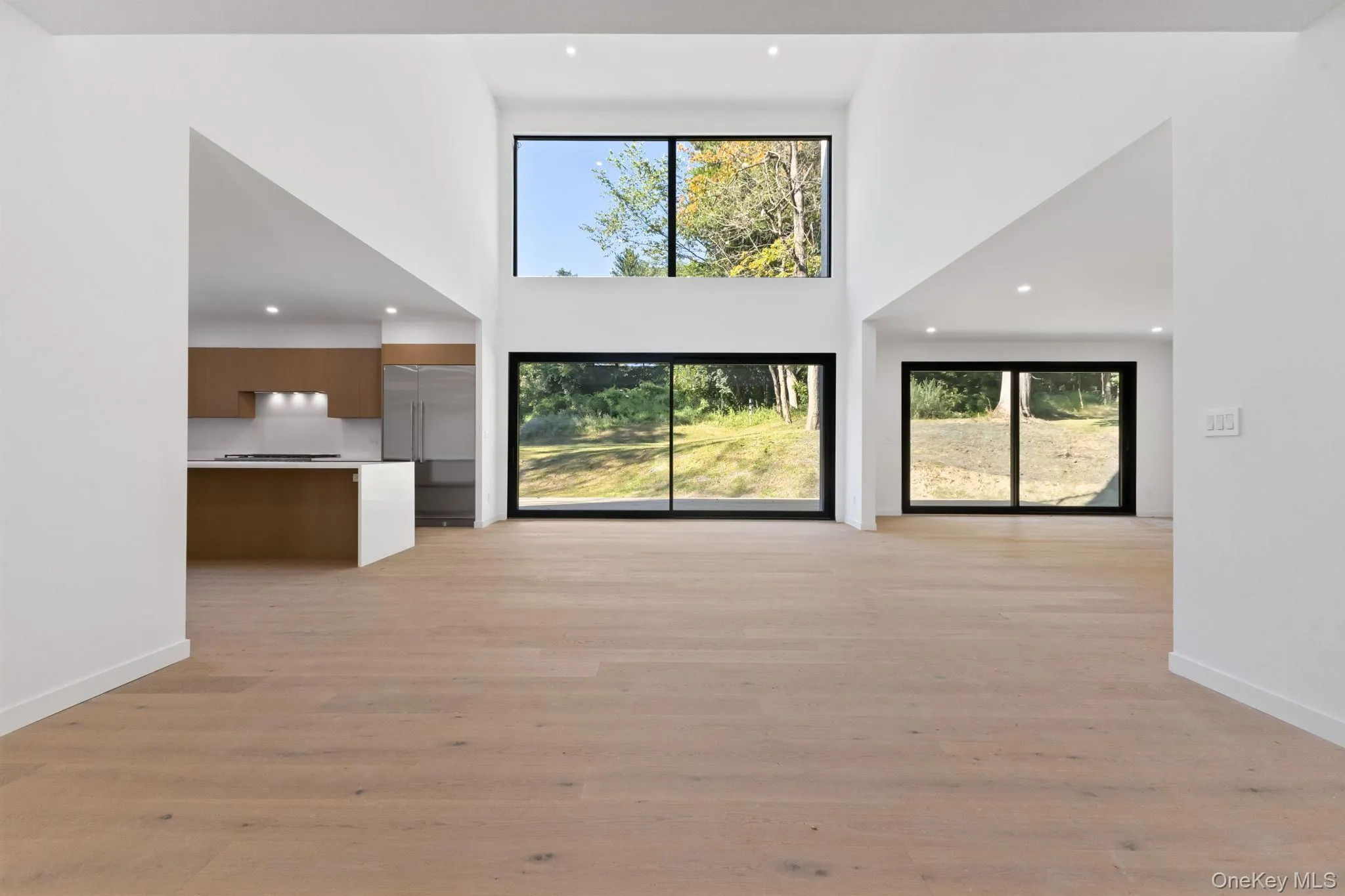 Unfurnished living room with healthy amount of natural light, recessed lighting, light wood-style floors, and a towering ceiling Unfurnished living room with healthy amount of natural light, recessed lighting, light wood-style floors, and a towering ceiling