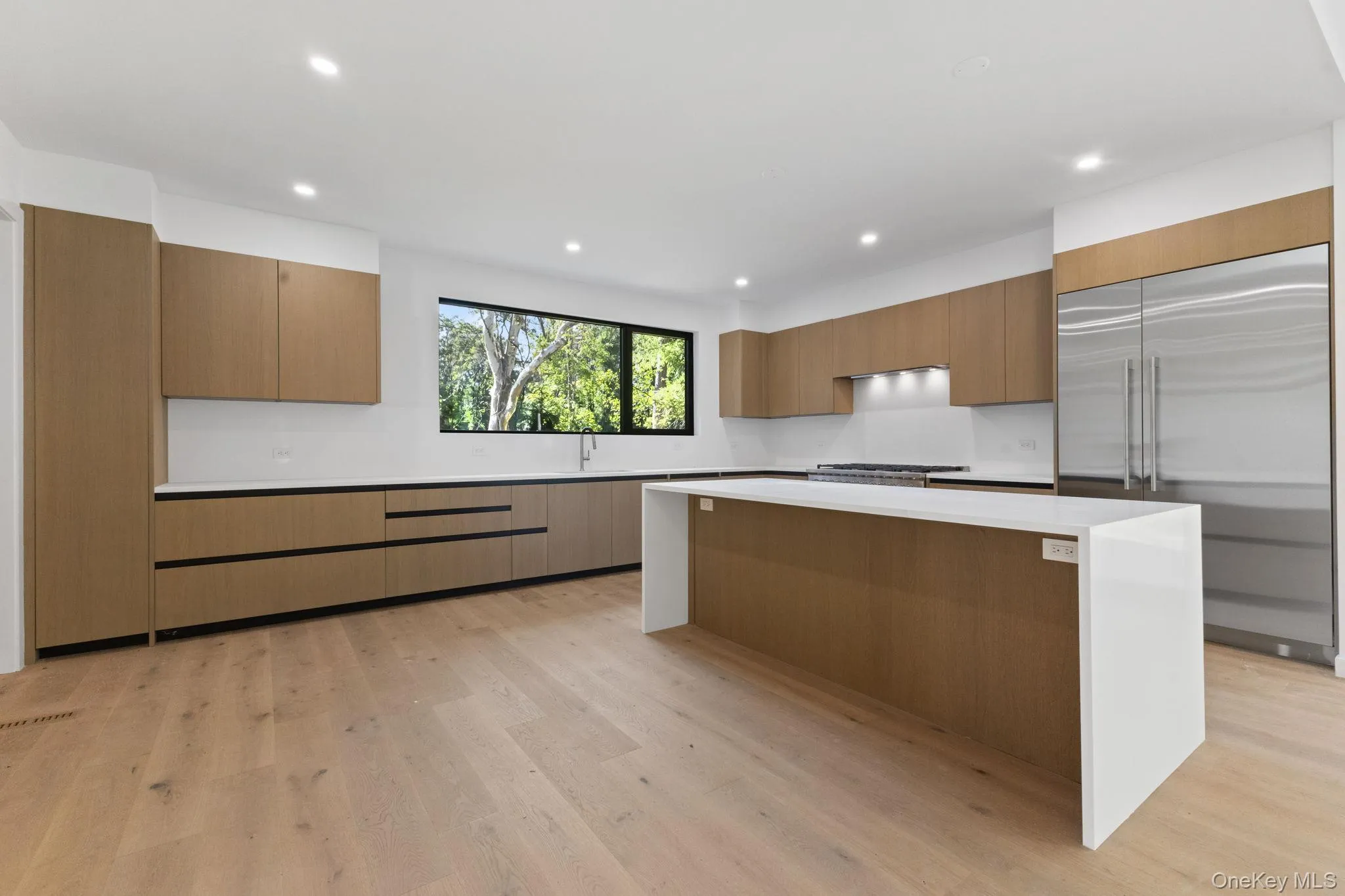 Kitchen featuring built in refrigerator, brown cabinetry, light wood-style floors, a kitchen island, and light stone counters Kitchen featuring built in refrigerator, brown cabinetry, light wood-style floors, a kitchen island, and light stone counters