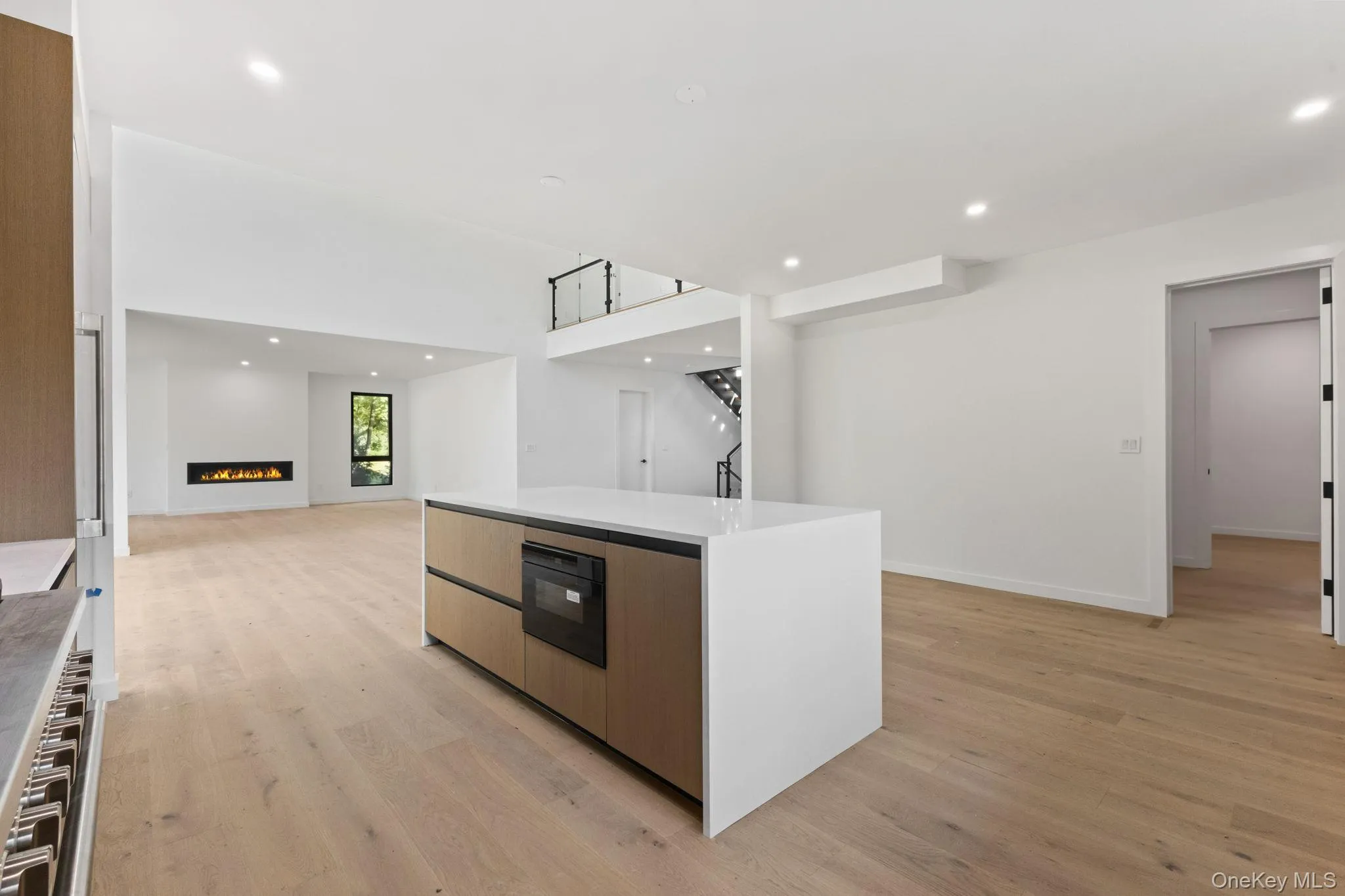 Kitchen featuring a lit fireplace, recessed lighting, modern cabinets, light wood-style flooring, and light stone countertops Kitchen featuring a lit fireplace, recessed lighting, modern cabinets, light wood-style flooring, and light stone countertops