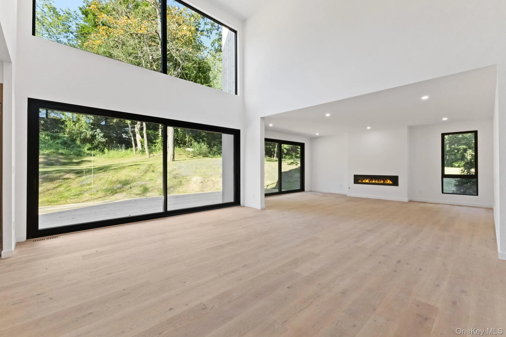 Unfurnished living room with a lit fireplace, light wood-style flooring, recessed lighting, and a high ceiling Unfurnished living room with a lit fireplace, light wood-style flooring, recessed lighting, and a high ceiling