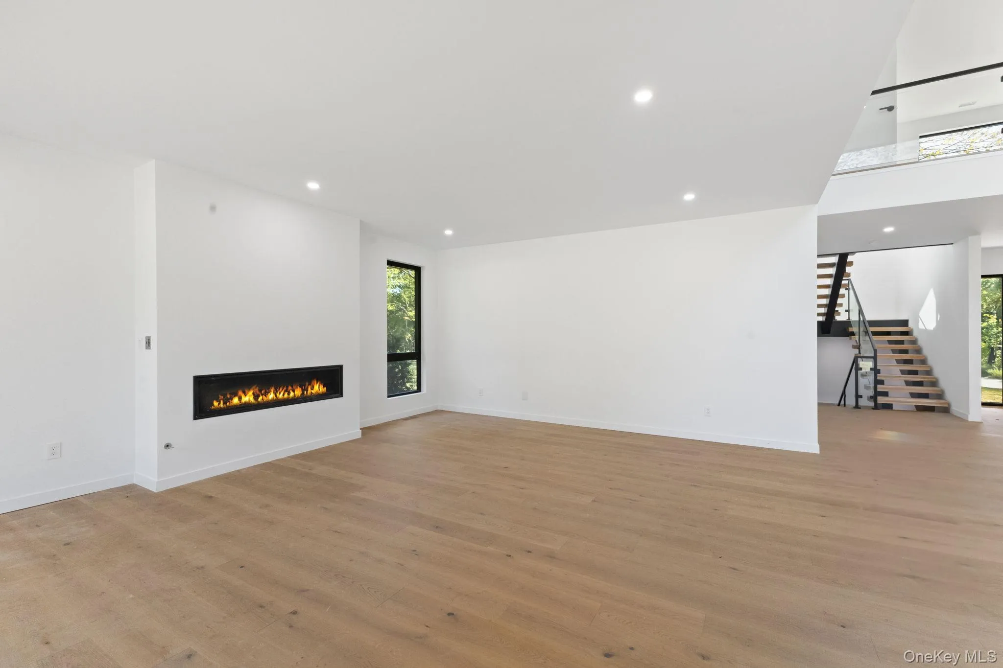Unfurnished living room with healthy amount of natural light, recessed lighting, a glass covered fireplace, light wood finished floors, and stairway Unfurnished living room with healthy amount of natural light, recessed lighting, a glass covered fireplace, light wood finished floors, and stairway