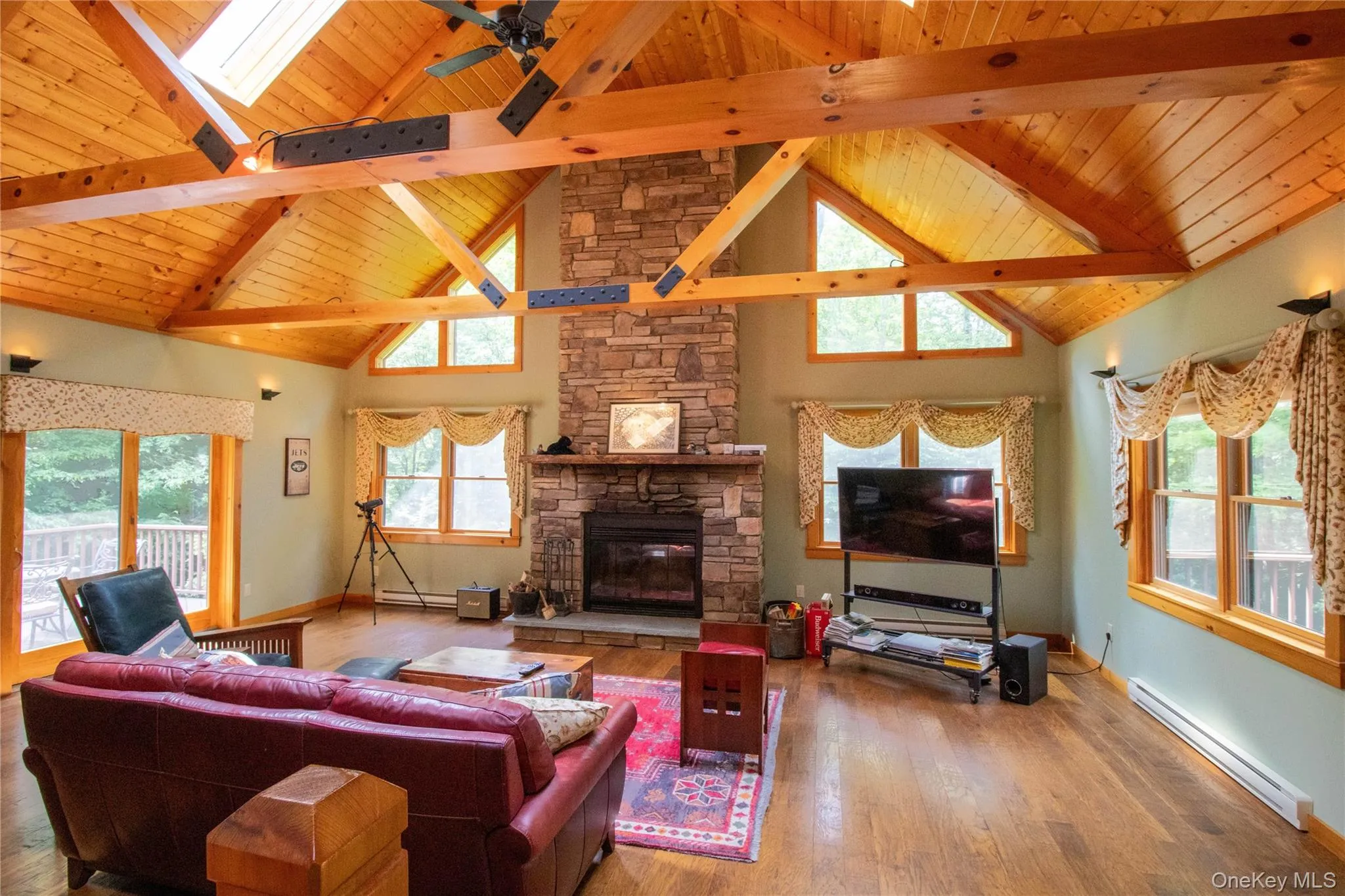 Living area featuring a baseboard radiator, high vaulted ceiling, wood finished floors, a fireplace, and a skylight Living area featuring a baseboard radiator, high vaulted ceiling, wood finished floors, a fireplace, and a skylight
