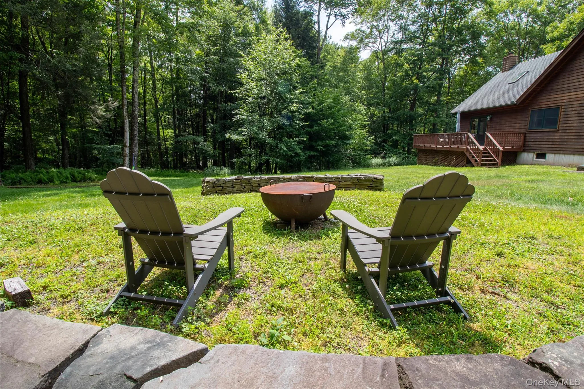 View of grassy yard featuring an outdoor fire pit, a wooden deck, and stairway View of grassy yard featuring an outdoor fire pit, a wooden deck, and stairway