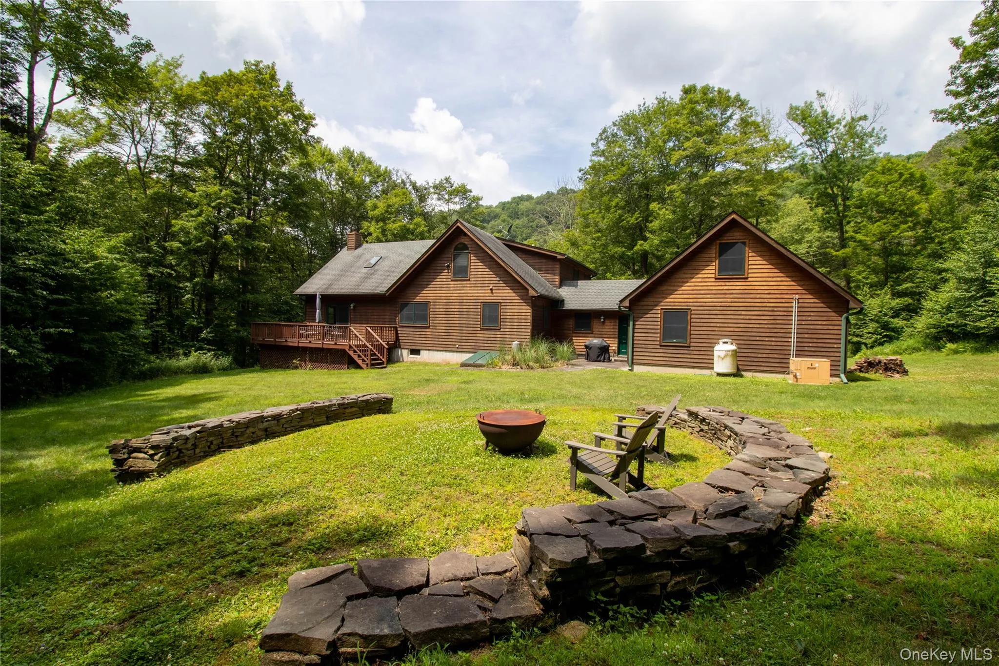 Back of property with a deck, a lawn, a chimney, a forest view, and an outdoor fire pit Back of property with a deck, a lawn, a chimney, a forest view, and an outdoor fire pit