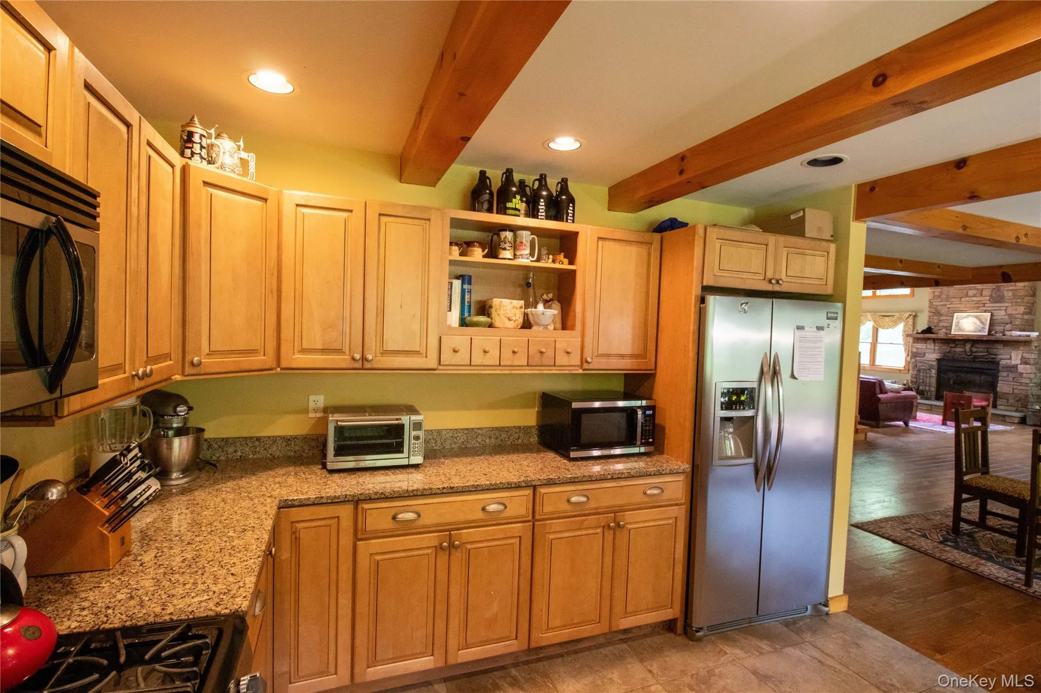 Kitchen with beam ceiling, open shelves, appliances with stainless steel finishes, light stone counters, and a fireplace Kitchen with beam ceiling, open shelves, appliances with stainless steel finishes, light stone counters, and a fireplace