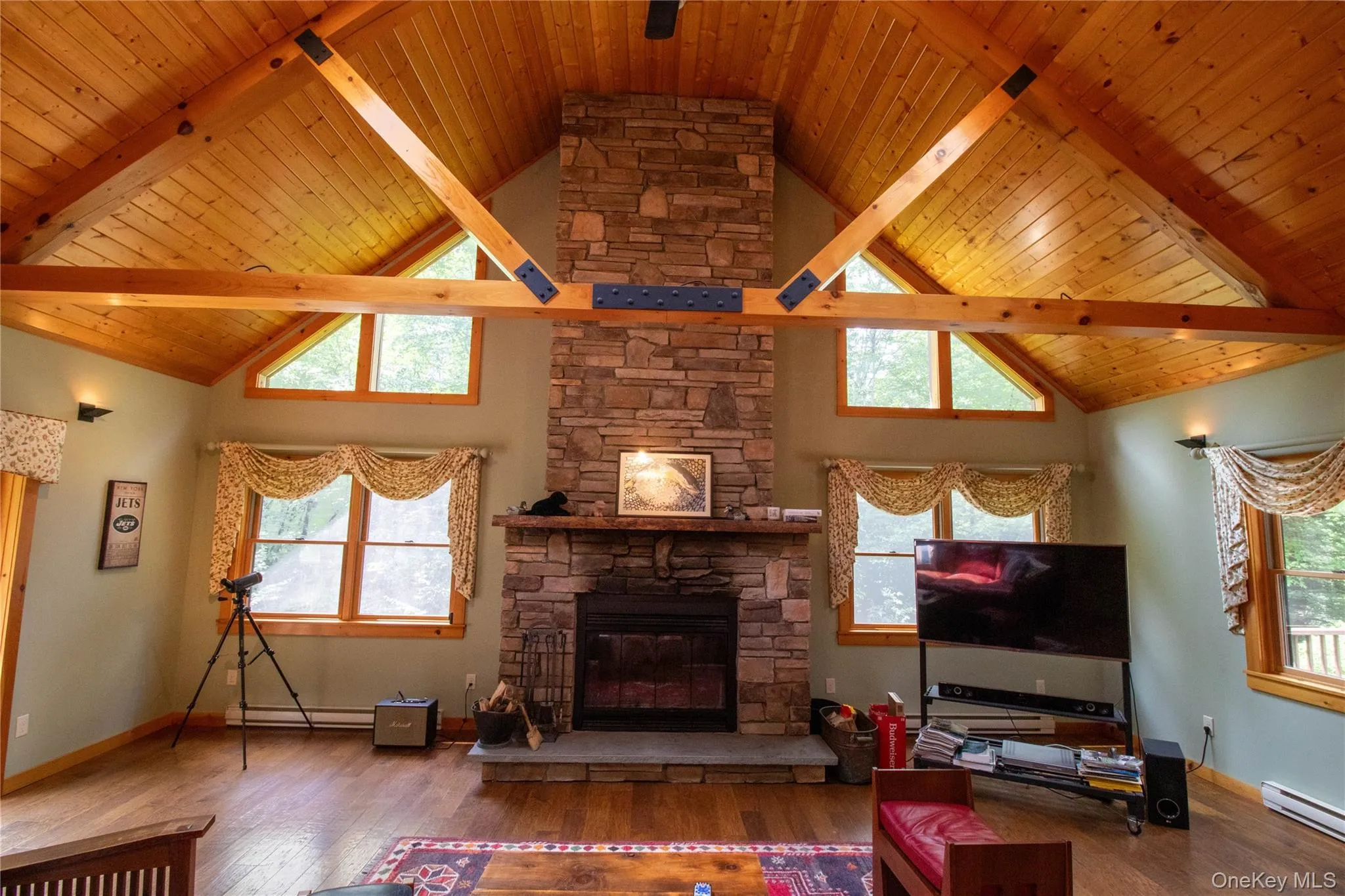 Living area with wood-type flooring, high vaulted ceiling, a wood ceiling with exposed beams, a fireplace, and baseboard heating Living area with wood-type flooring, high vaulted ceiling, a wood ceiling with exposed beams, a fireplace, and baseboard heating