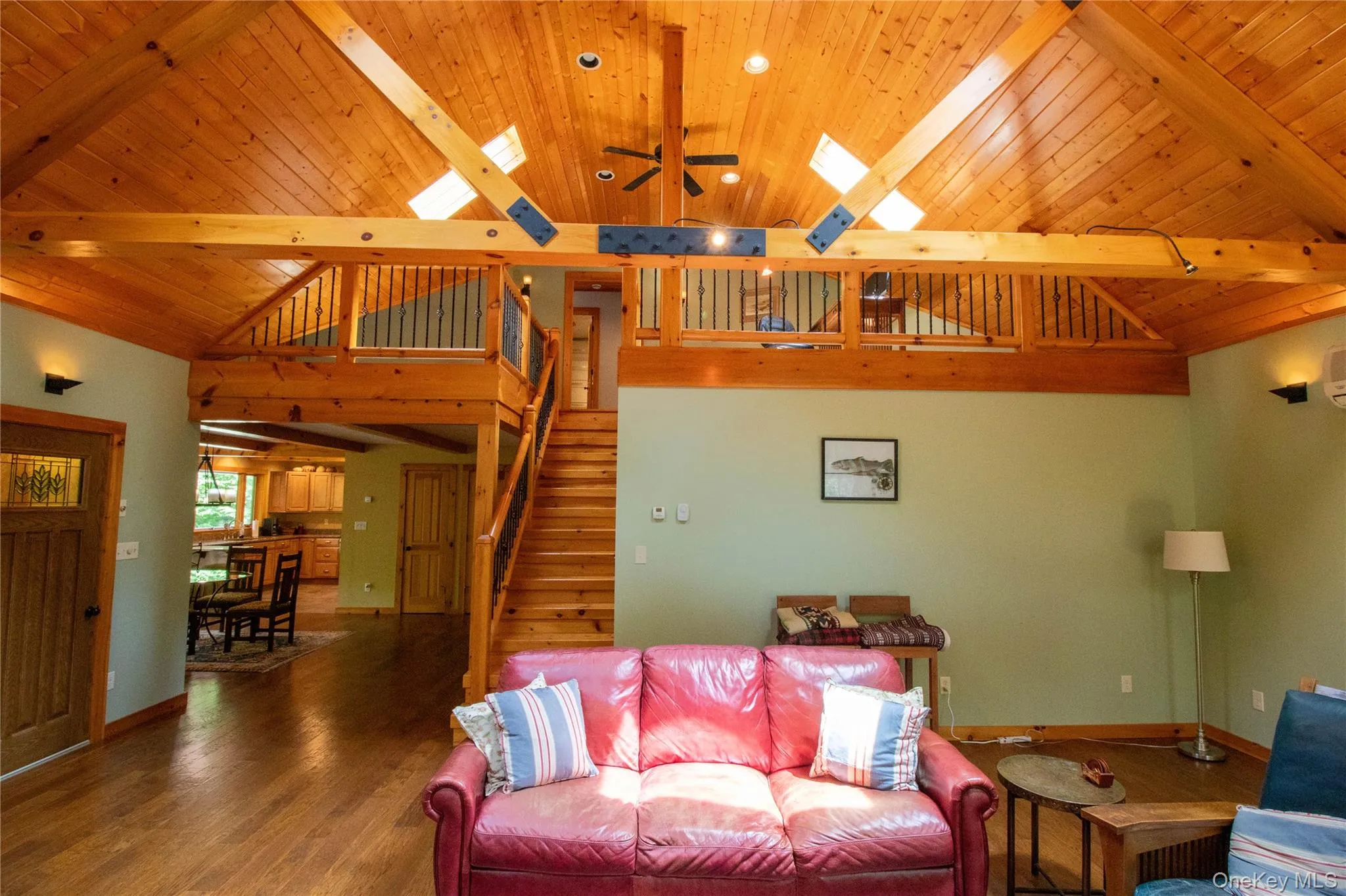 Living room with a ceiling fan, a wood ceiling with exposed beams, wood finished floors, stairs, and high vaulted ceiling Living room with a ceiling fan, a wood ceiling with exposed beams, wood finished floors, stairs, and high vaulted ceiling