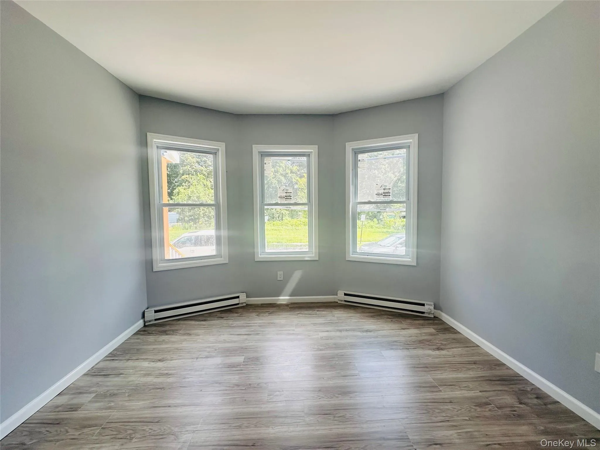 Unfurnished room with baseboard heating and light wood-style floors Unfurnished room with baseboard heating and light wood-style floors