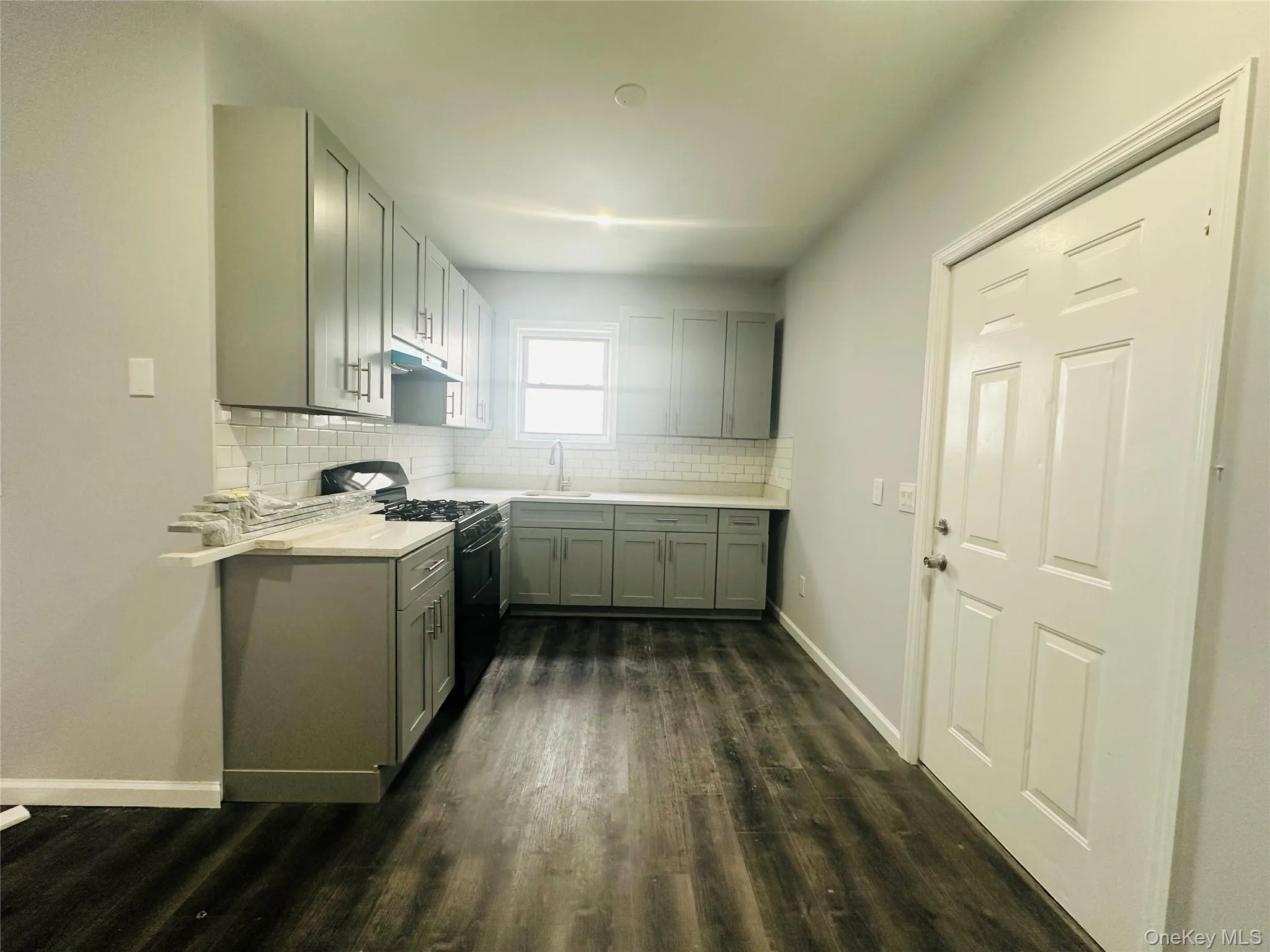 Kitchen with black gas range, dark wood finished floors, gray cabinetry, and backsplash Kitchen with black gas range, dark wood finished floors, gray cabinetry, and backsplash