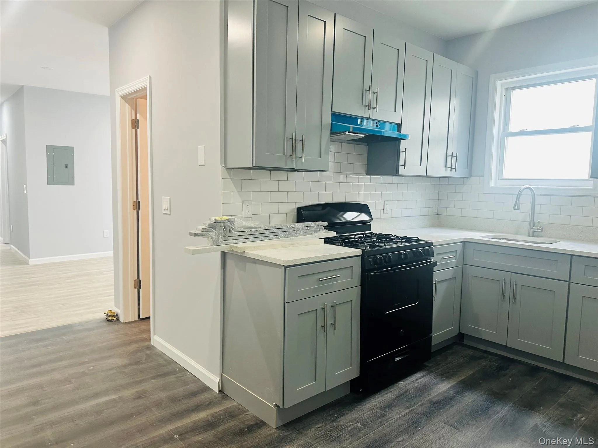 Kitchen featuring black gas range oven, dark wood-style floors, backsplash, under cabinet range hood, and light stone countertops Kitchen featuring black gas range oven, dark wood-style floors, backsplash, under cabinet range hood, and light stone countertops