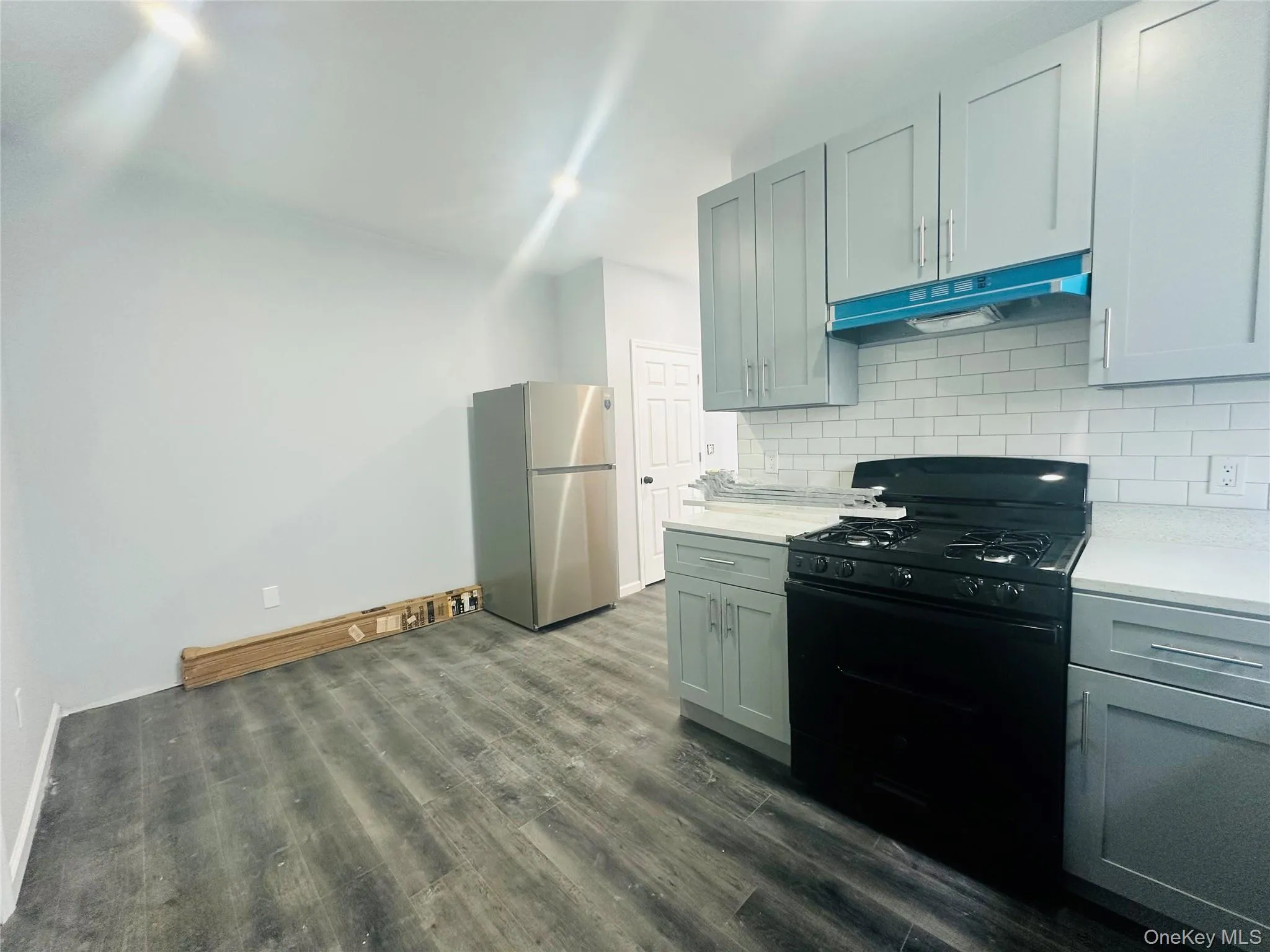 Kitchen with black gas stove, freestanding refrigerator, under cabinet range hood, tasteful backsplash, and dark wood-style floors Kitchen with black gas stove, freestanding refrigerator, under cabinet range hood, tasteful backsplash, and dark wood-style floors