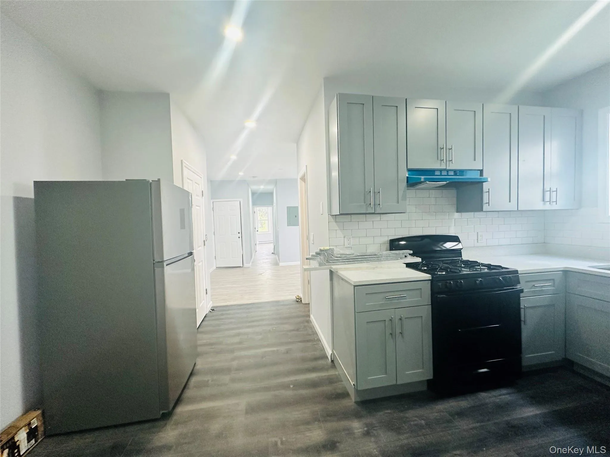 Kitchen with black gas stove, freestanding refrigerator, dark wood-type flooring, backsplash, and under cabinet range hood Kitchen with black gas stove, freestanding refrigerator, dark wood-type flooring, backsplash, and under cabinet range hood