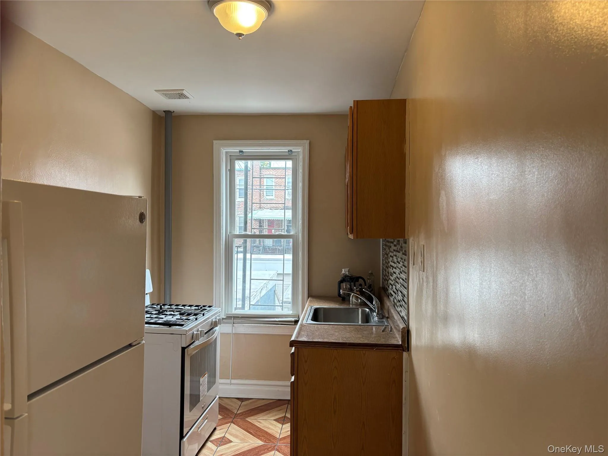 Kitchen featuring freestanding refrigerator, gas range oven, brown cabinets, decorative backsplash, and dark countertops Kitchen featuring freestanding refrigerator, gas range oven, brown cabinets, decorative backsplash, and dark countertops