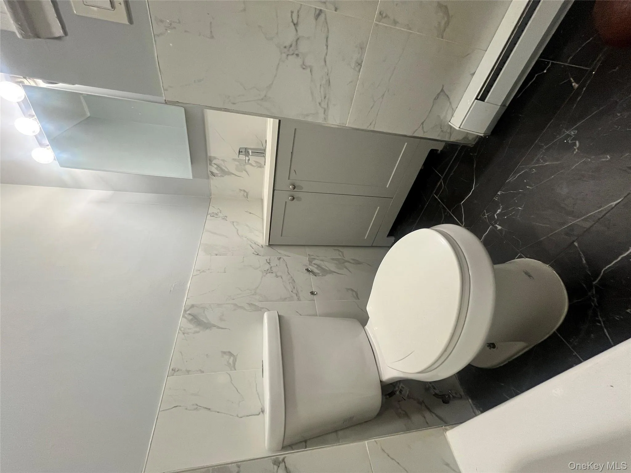 Half bath with dark marble finish flooring, tile walls, a baseboard heating unit, vanity, and wainscoting Half bath with dark marble finish flooring, tile walls, a baseboard heating unit, vanity, and wainscoting