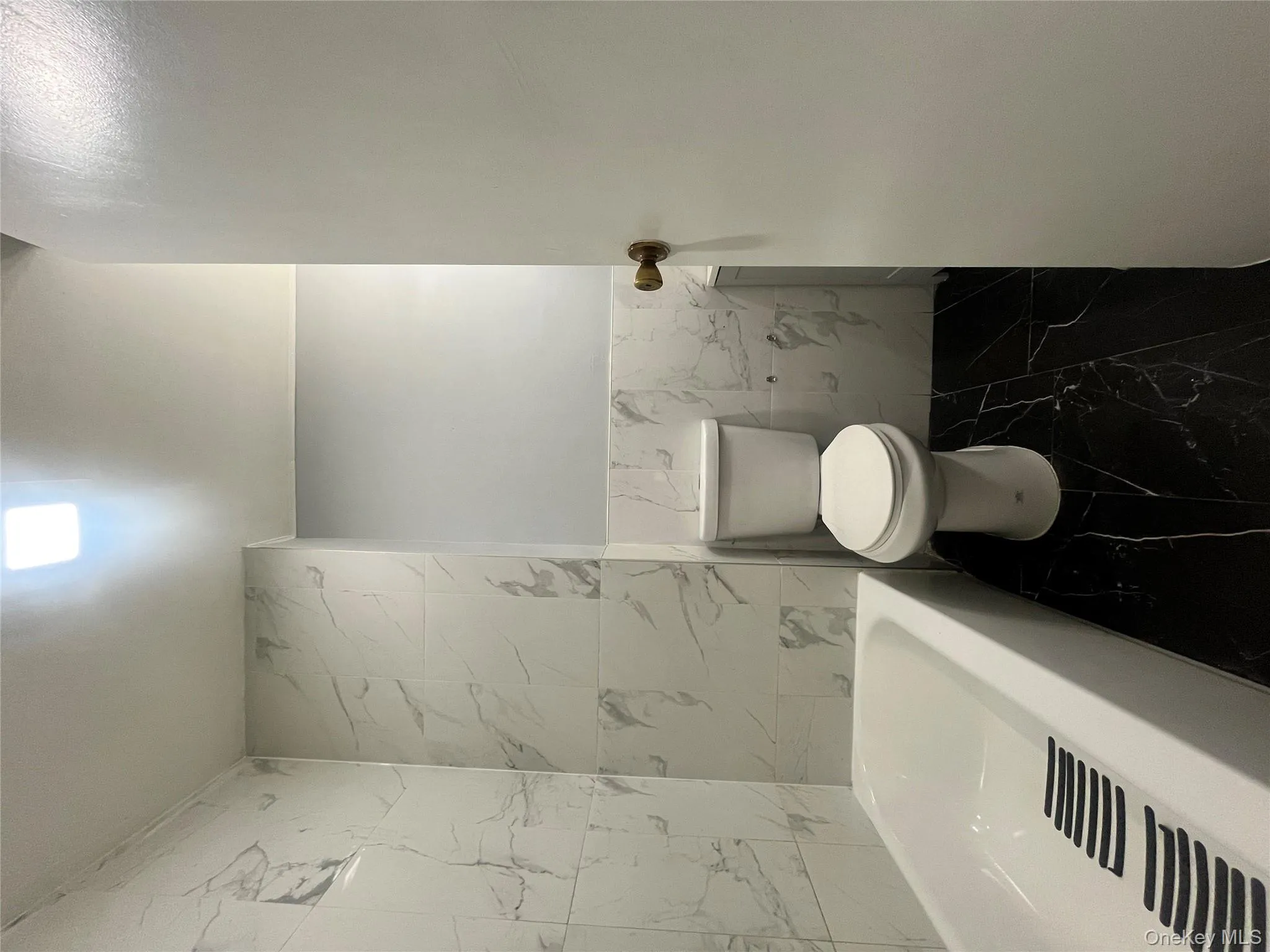 Full bathroom with tile walls, marble look tiles, and wainscoting Full bathroom with tile walls, marble look tiles, and wainscoting