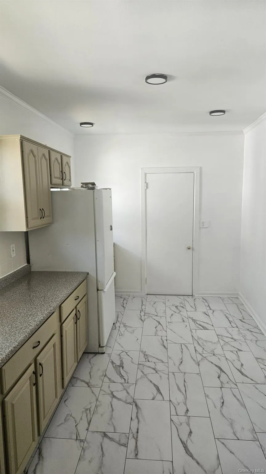 Kitchen featuring light marble finish flooring, dark countertops, ornamental molding, and freestanding refrigerator Kitchen featuring light marble finish flooring, dark countertops, ornamental molding, and freestanding refrigerator