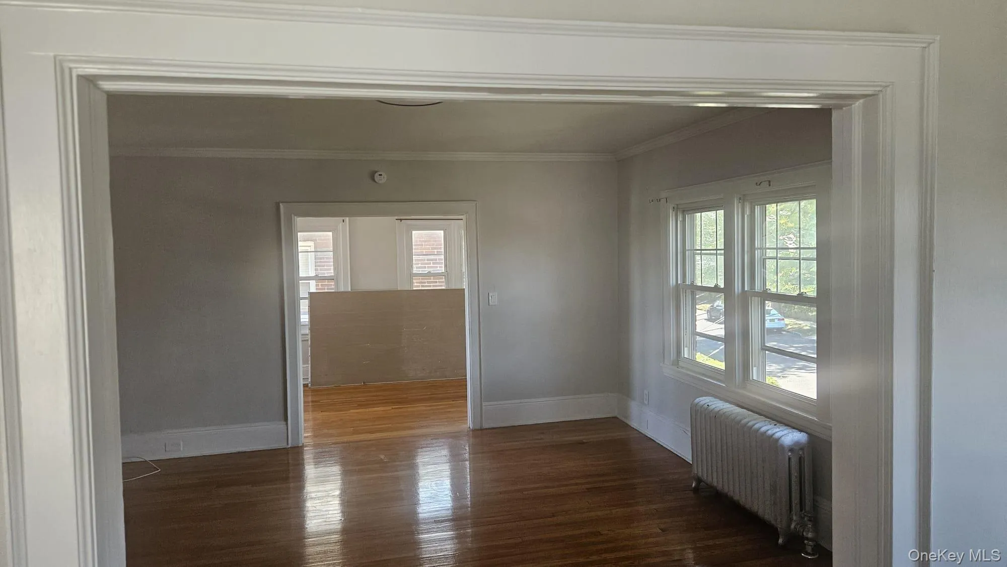 Empty room with radiator, dark wood-style floors, and crown molding Empty room with radiator, dark wood-style floors, and crown molding