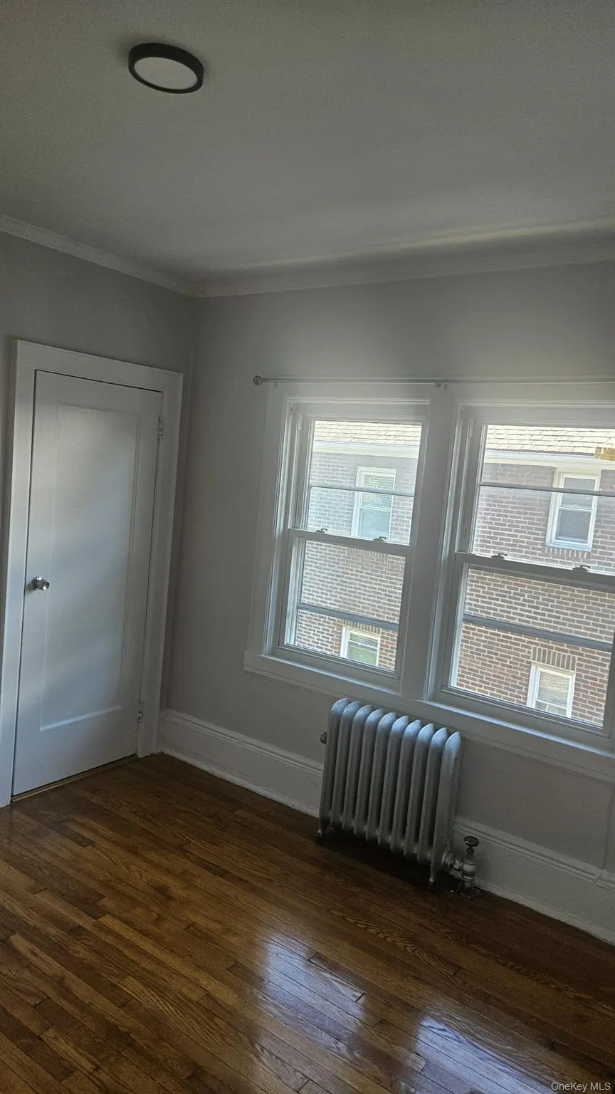 Unfurnished room featuring radiator, dark wood-style flooring, and ornamental molding Unfurnished room featuring radiator, dark wood-style flooring, and ornamental molding