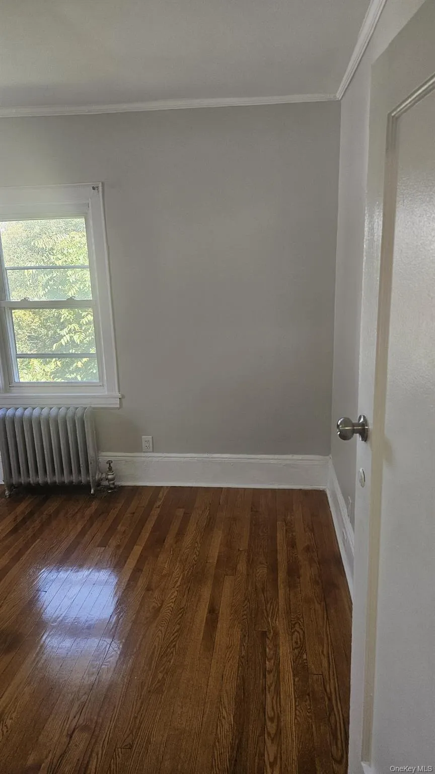 Unfurnished room with crown molding, radiator heating unit, and dark wood-style flooring Unfurnished room with crown molding, radiator heating unit, and dark wood-style flooring