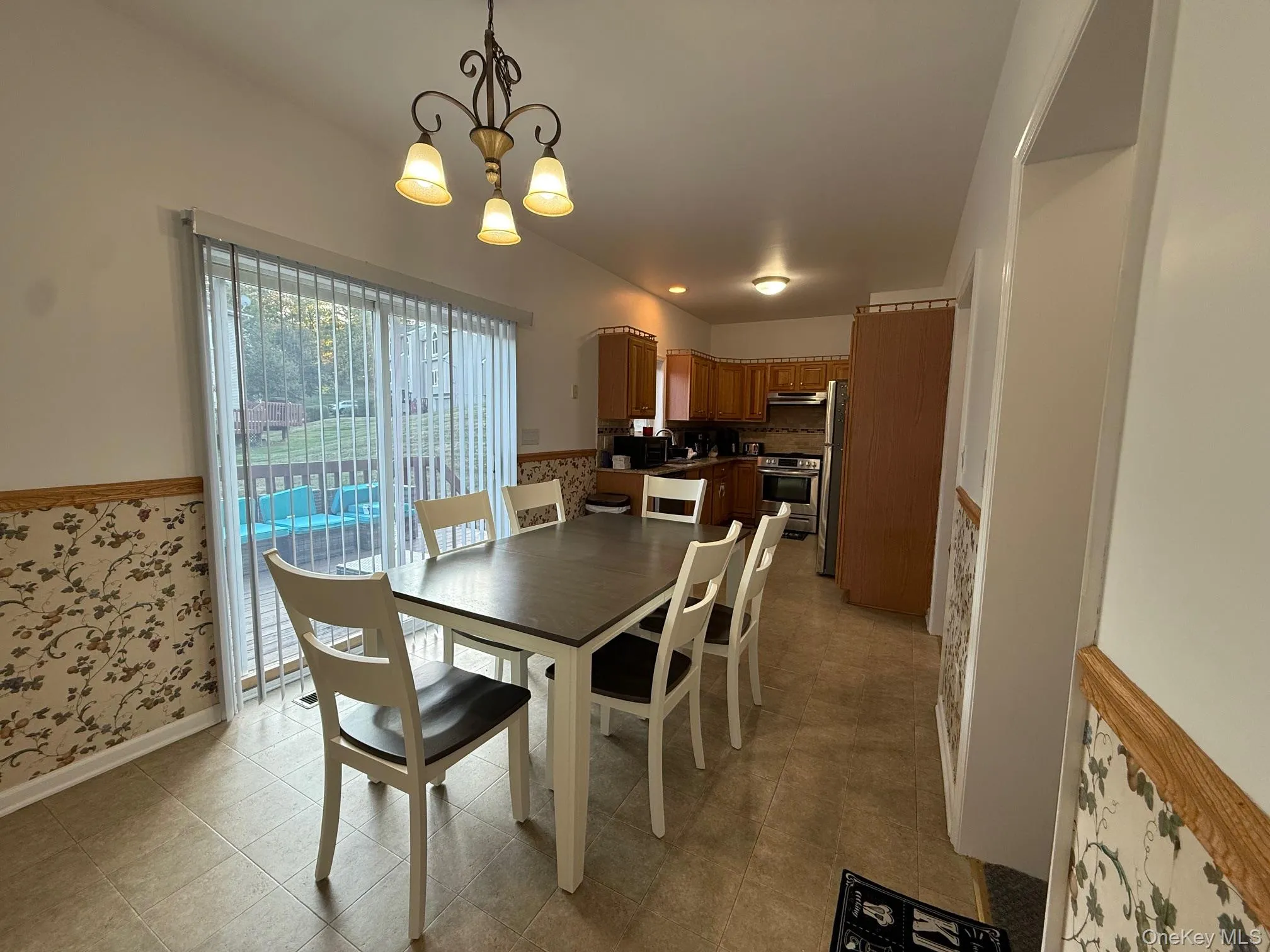 Dining room featuring a wainscoted wall, a chandelier, and wallpapered walls Dining room featuring a wainscoted wall, a chandelier, and wallpapered walls