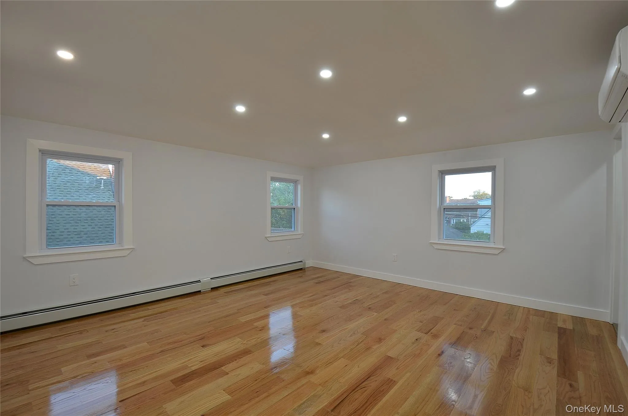 Bedroom featuring recessed lighting, a baseboard radiator, light wood finished floors, and a wall mounted AC Bedroom featuring recessed lighting, a baseboard radiator, light wood finished floors, and a wall mounted AC