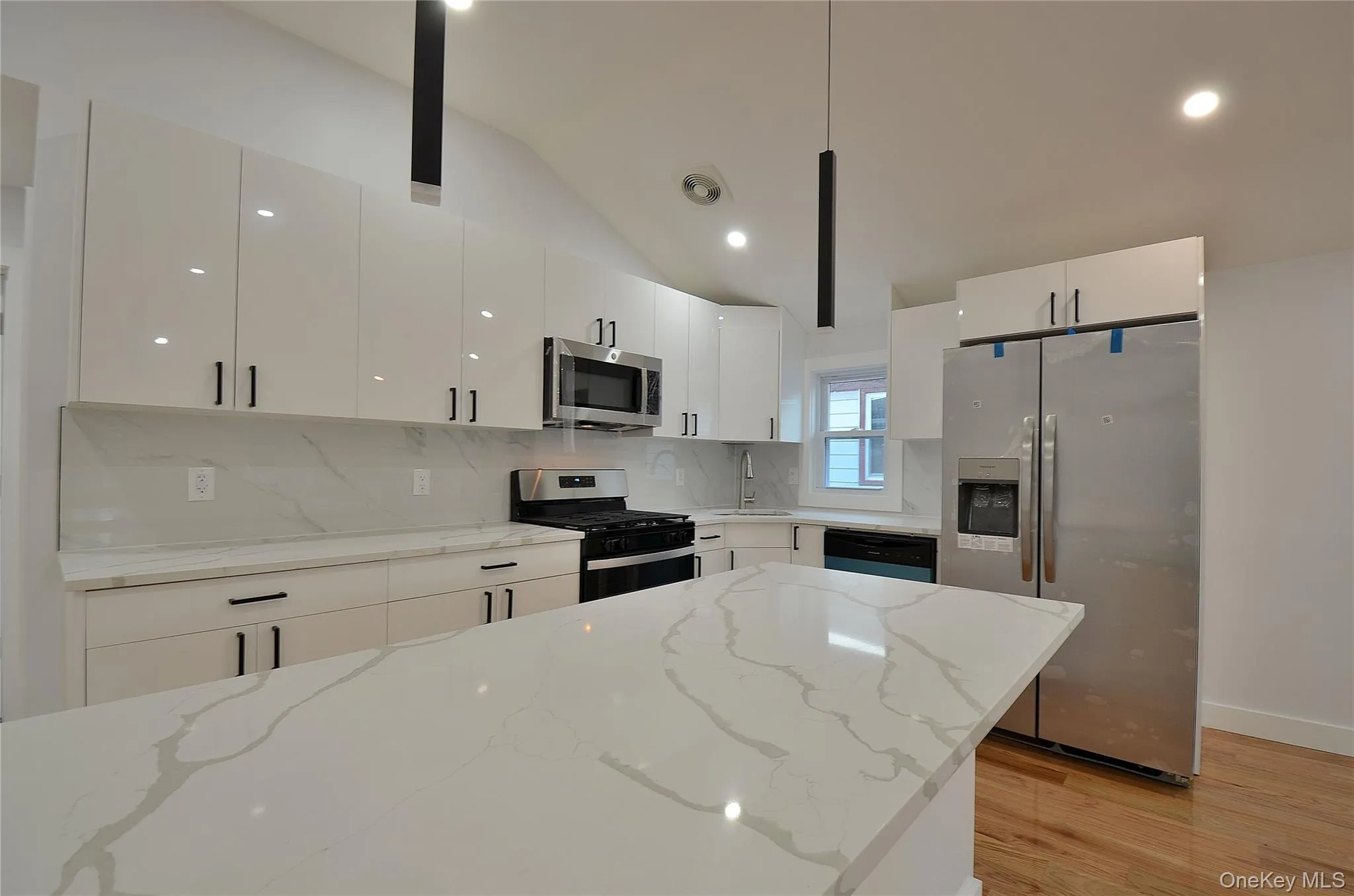 Kitchen featuring stainless steel appliances, vaulted ceiling, tasteful backsplash, light stone counters, and white cabinets Kitchen featuring stainless steel appliances, vaulted ceiling, tasteful backsplash, light stone counters, and white cabinets