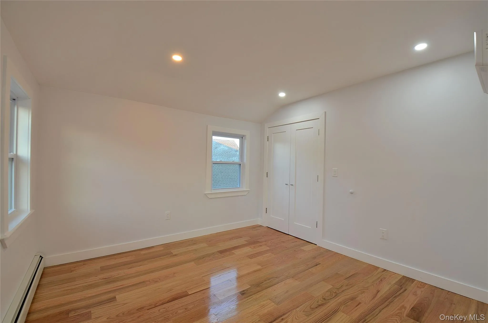 Bedroom featuring a baseboard radiator, vaulted ceiling, recessed lighting, and light wood-type flooring Bedroom featuring a baseboard radiator, vaulted ceiling, recessed lighting, and light wood-type flooring