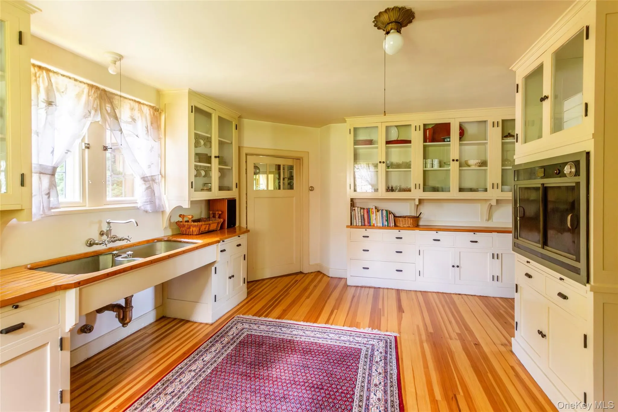 Kitchen with glass insert cabinets, white cabinets, and light wood-style flooring Kitchen with glass insert cabinets, white cabinets, and light wood-style flooring